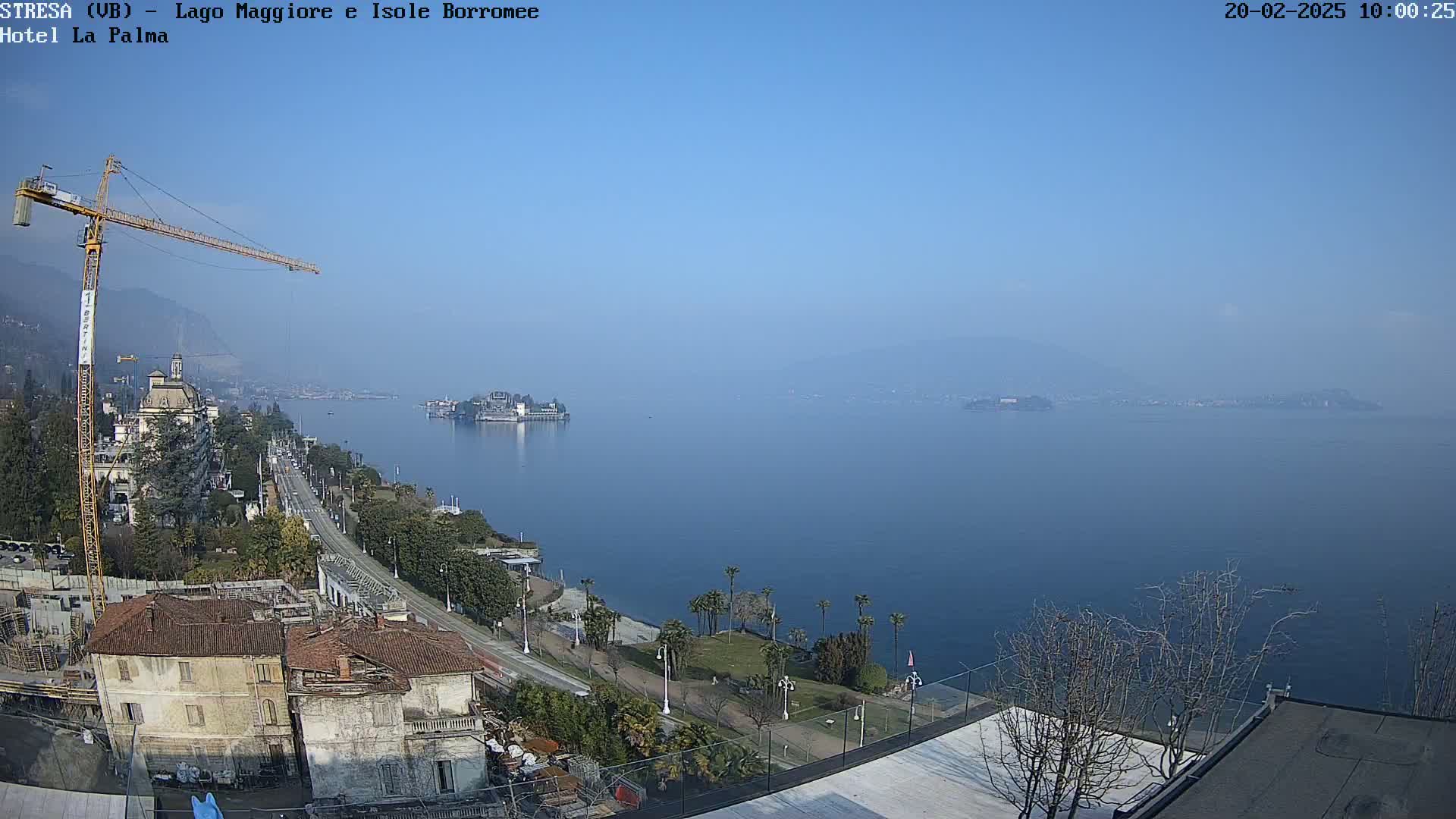 A clear, sunny day overlooks a large body of water with islands in the distance, a town along the shoreline, and a construction crane.
