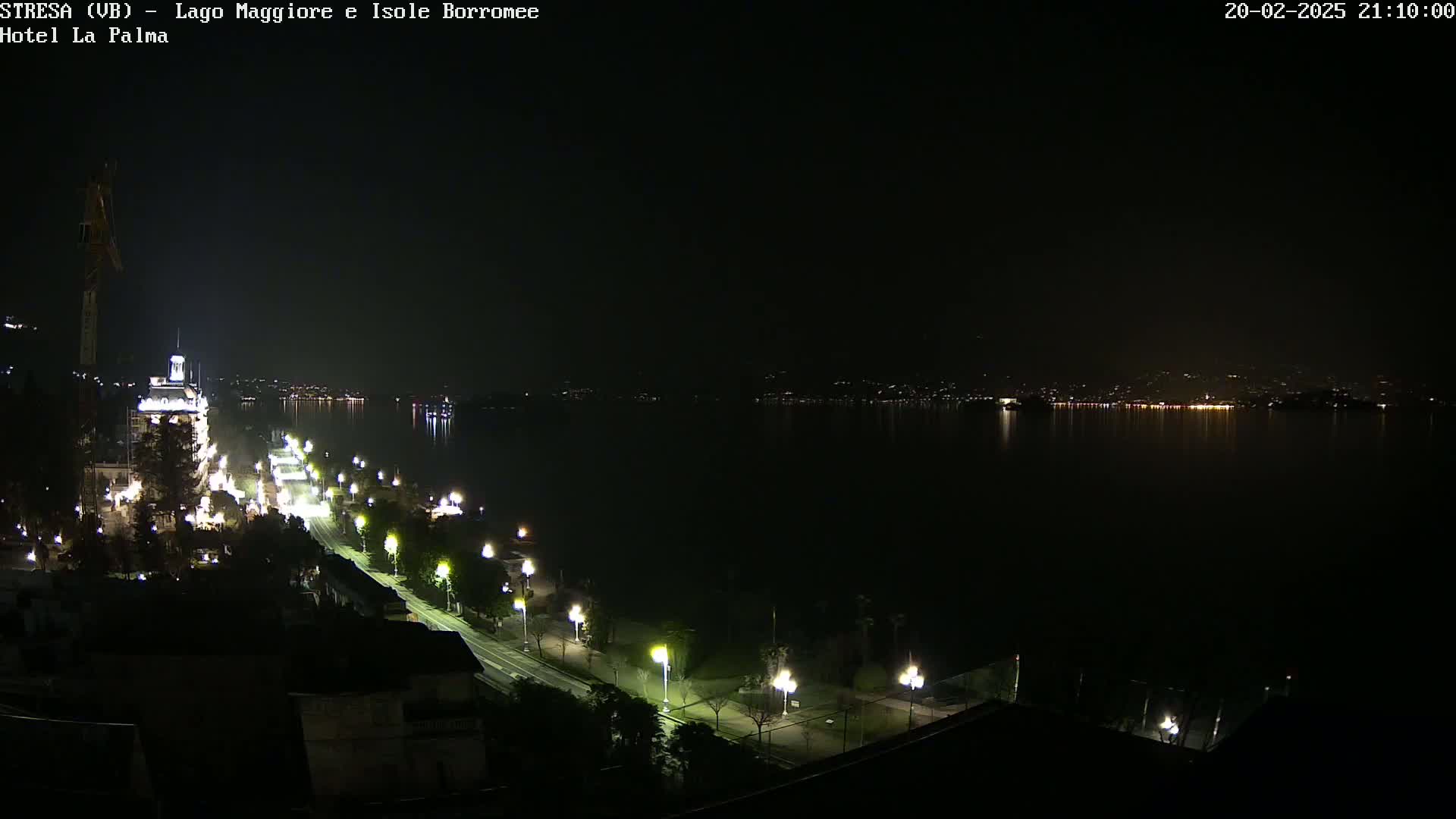 A nighttime view of a city's illuminated waterfront along a calm lake, with distant lights on the opposite shore.