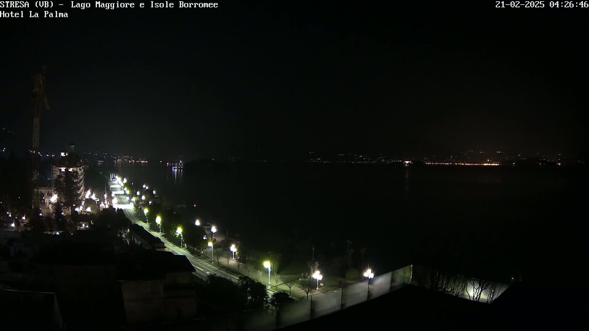 A nighttime, long shot of a city road illuminated by streetlights alongside a dark body of water, with faintly visible lights across the water.