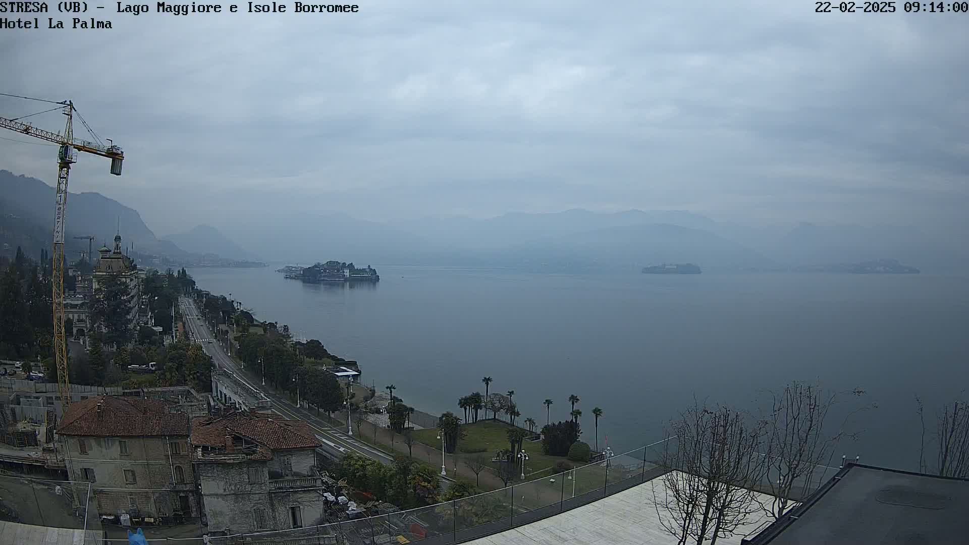 A cloudy day overlooking a large lake with islands in the distance, a town along the shoreline, and a construction crane visible near buildings under construction.