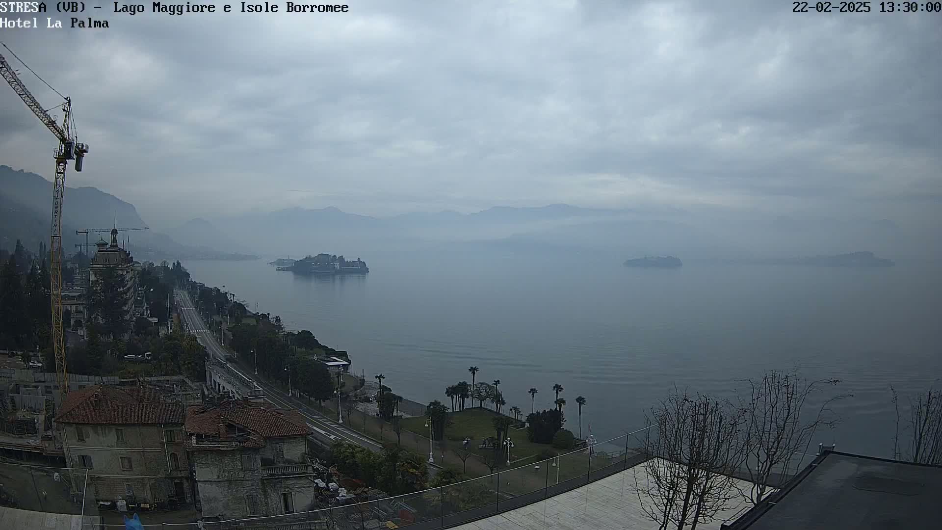 A hazy, overcast day reveals a view of a lake with islands in the distance, a shoreline with buildings and trees, and a construction crane.