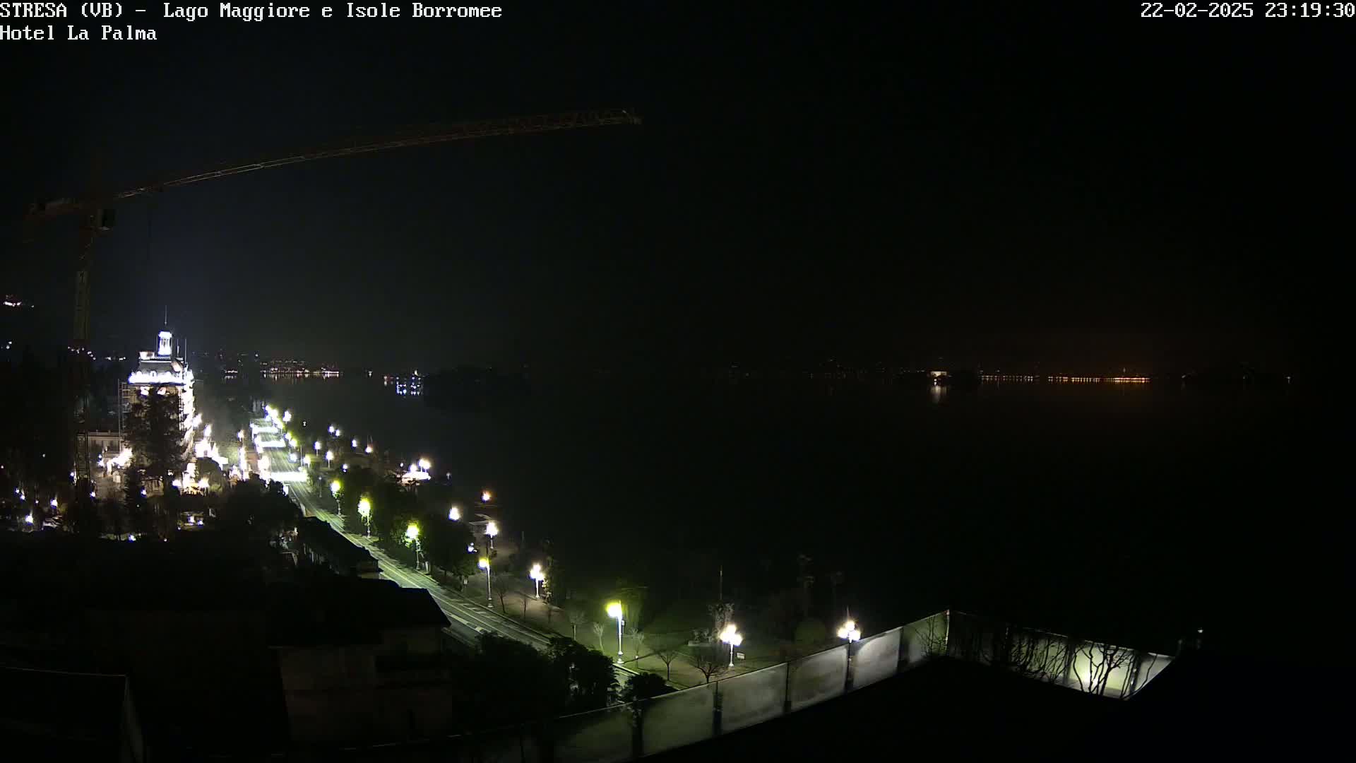 A nighttime, long shot of a city street and waterfront illuminated by streetlights, overlooking a dark body of water with lights faintly visible on the opposite shore.