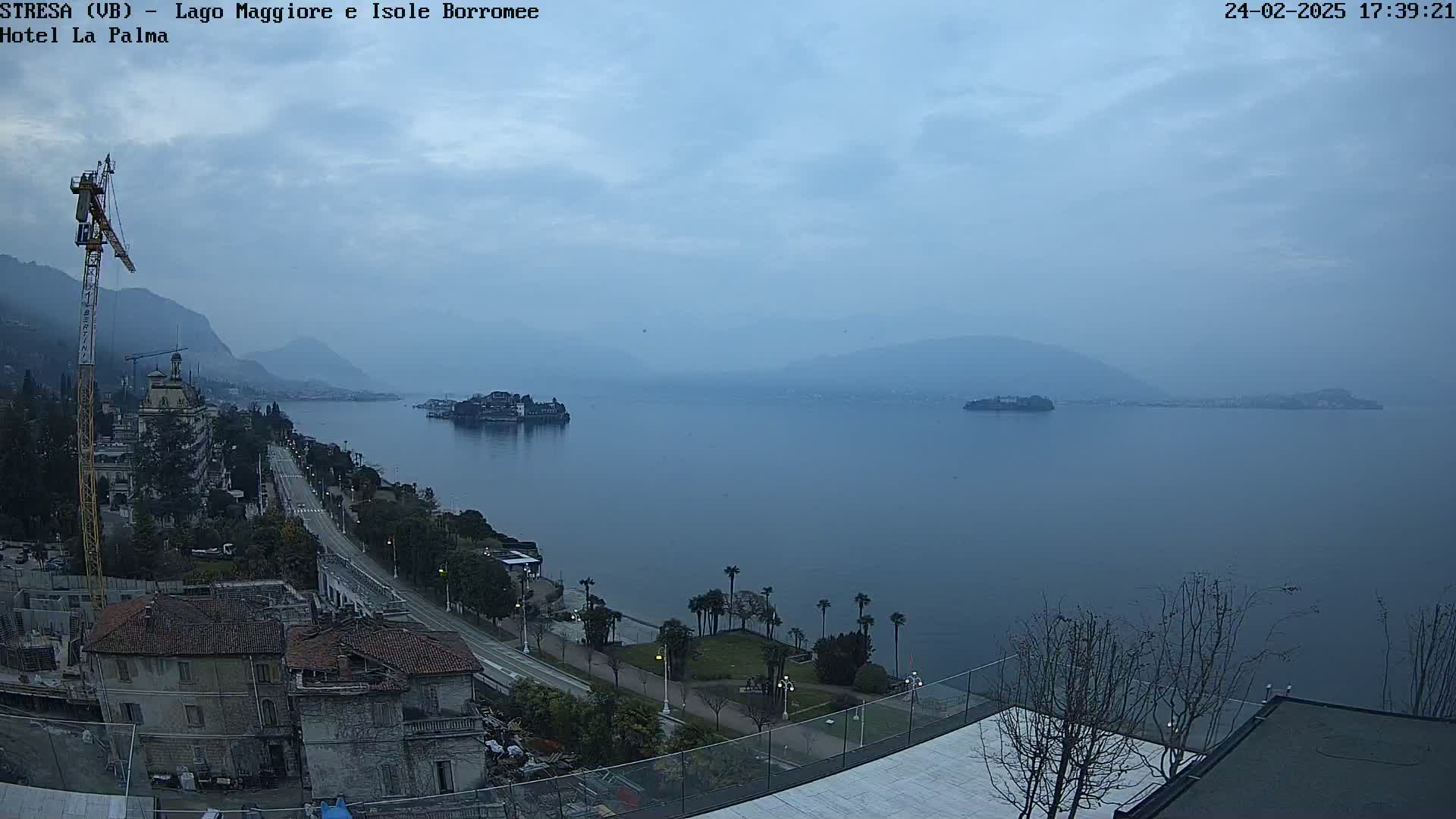 A hazy, overcast view of a lake, with islands and a shoreline featuring buildings and a road, is seen from an elevated vantage point.