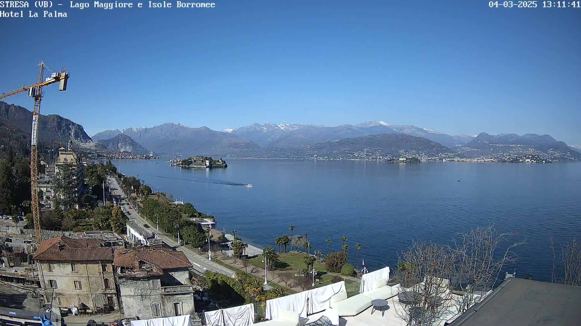 A sunny day overlooking a large lake with snow-capped mountains in the distance, a small island in the foreground, and a town along the shoreline.