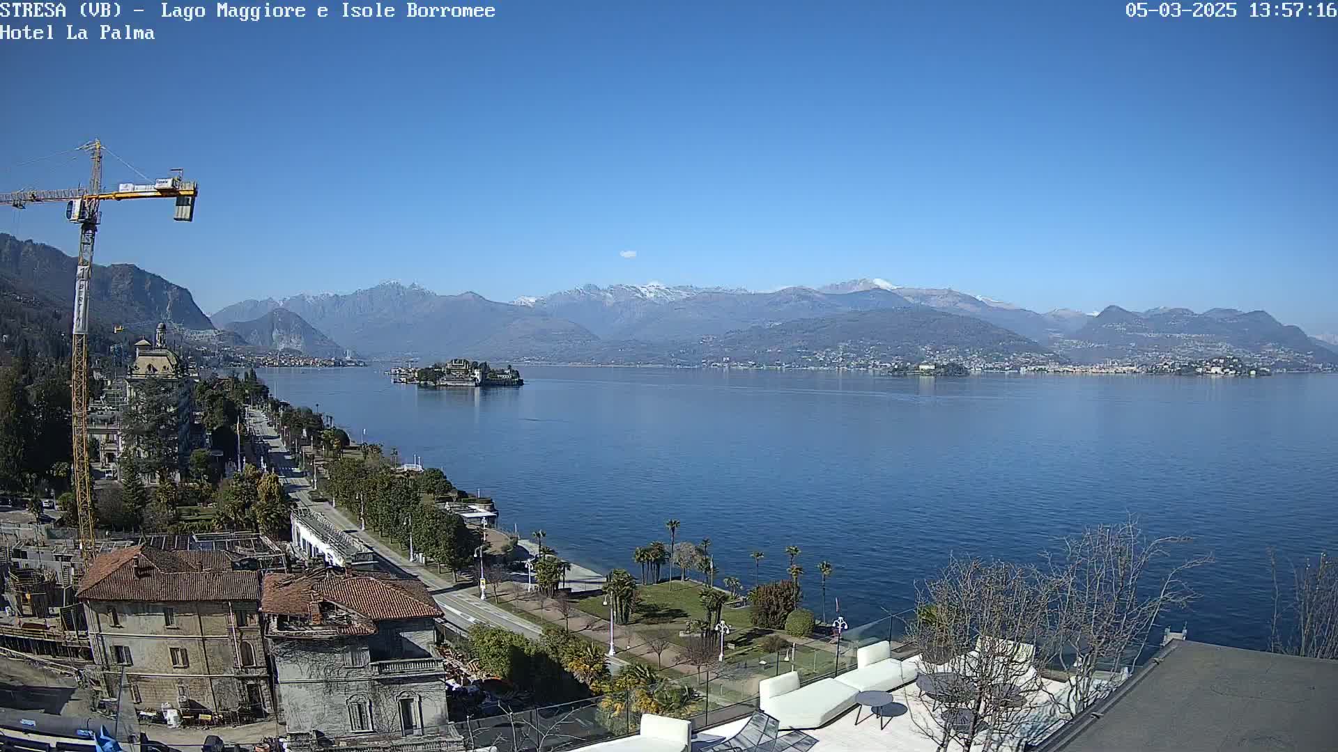 A sunny day overlooking a large lake with snow-capped mountains in the distance, a town on the lakeshore, and construction taking place near the foreground.