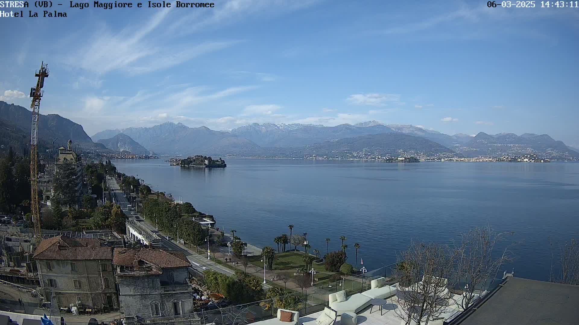 A clear, sunny day overlooks a large lake with snow-capped mountains in the background, a shoreline town, and a small island.