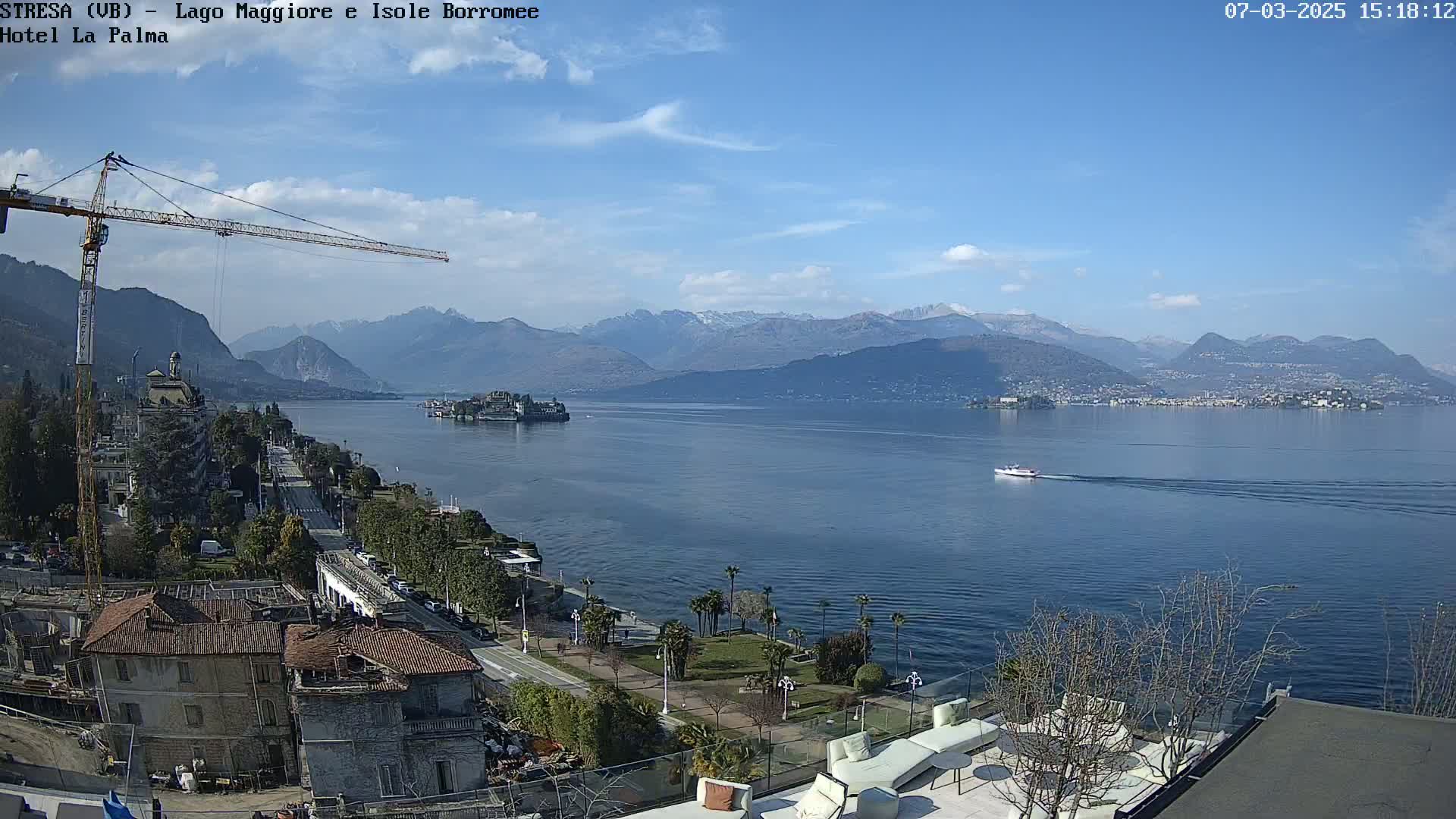 A sunny day overlooking a large lake with mountains in the background, a boat on the water, and construction underway near a building along the lakeshore.