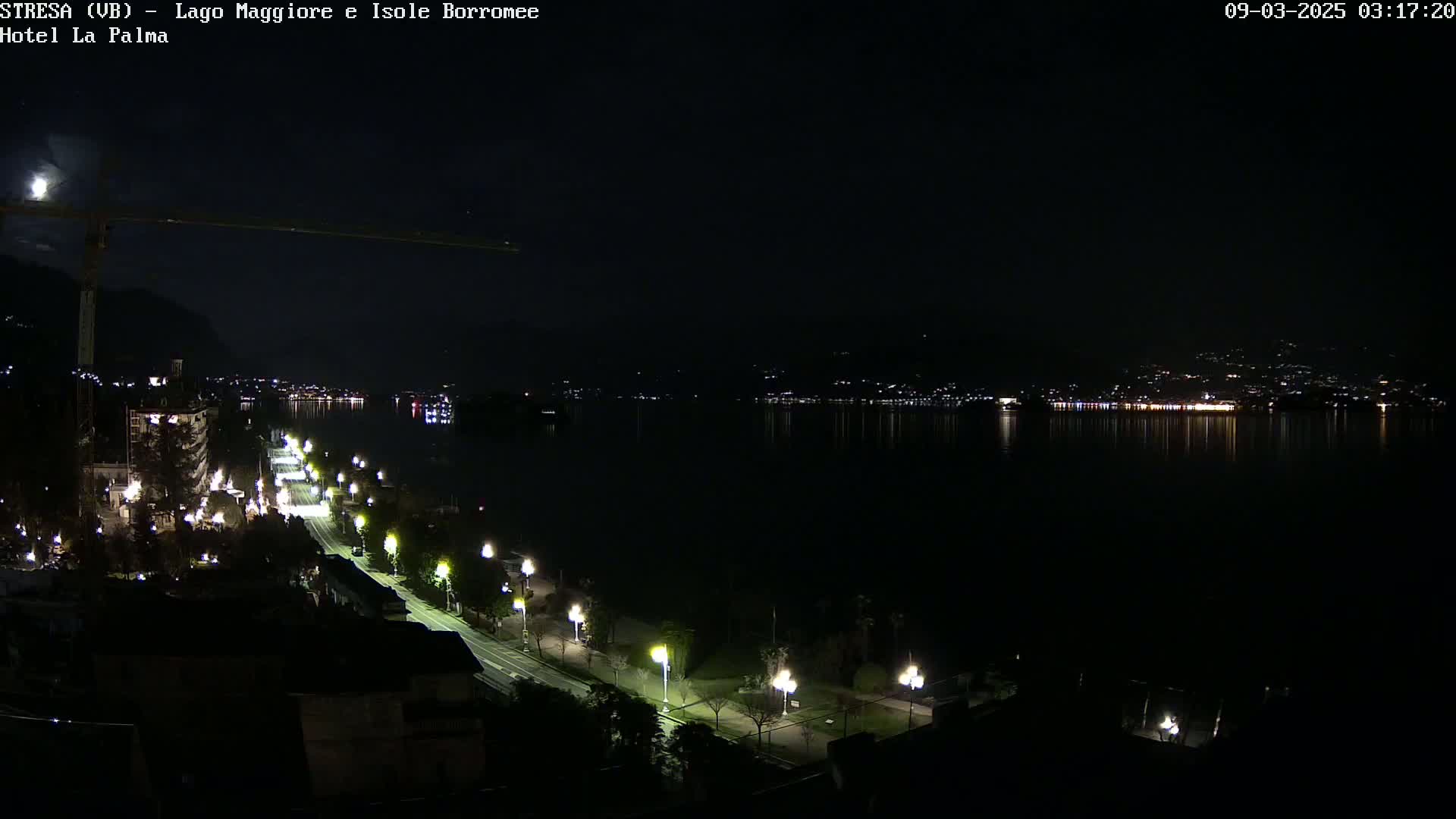 A nighttime view of a city's waterfront, featuring a calm lake reflecting city lights under a dark sky.