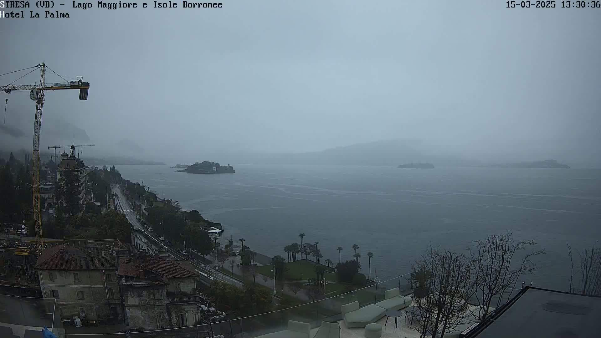 A rainy, overcast view of a lake and shoreline town, with a construction crane visible in the foreground.