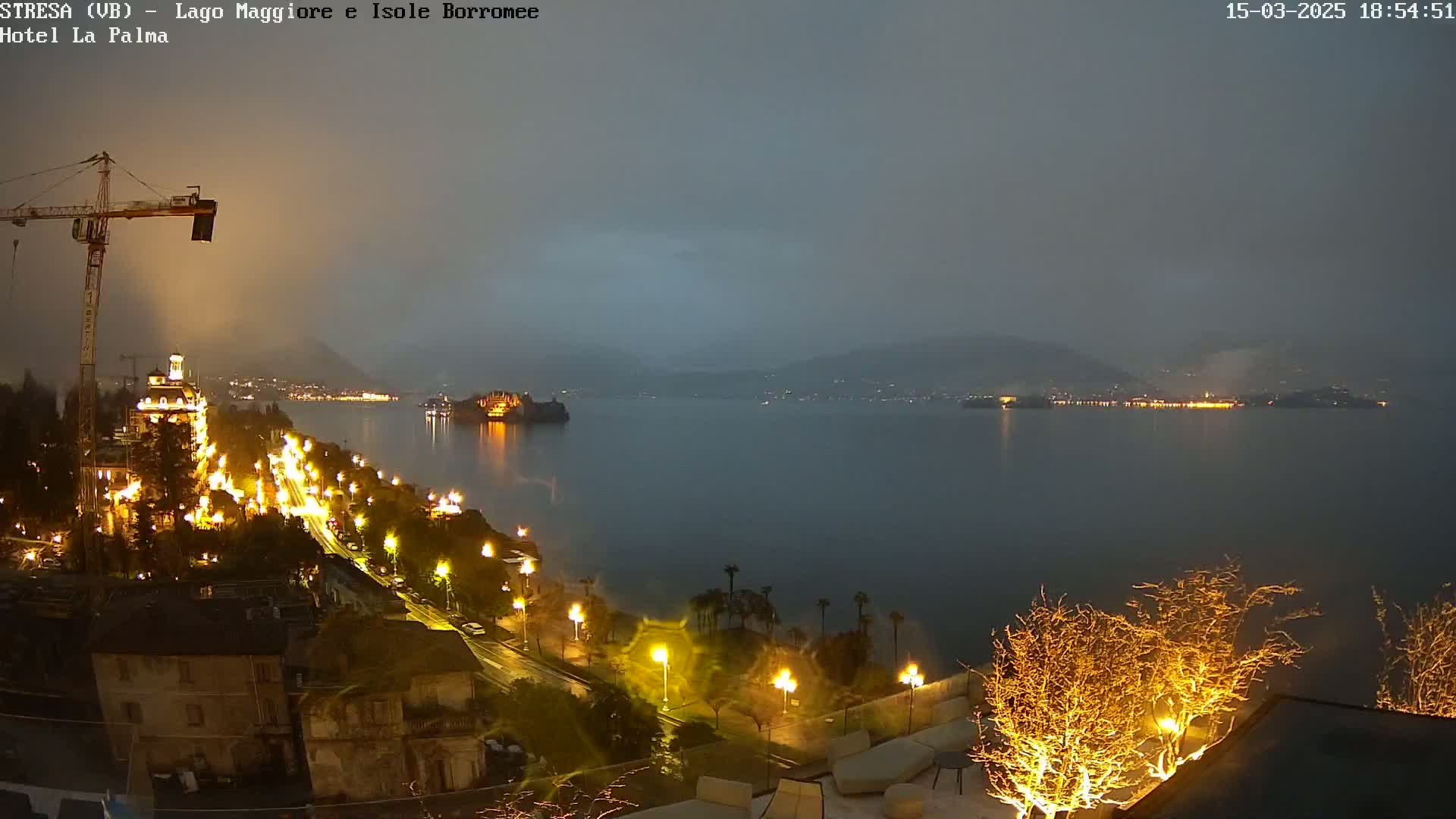 A nighttime view of a lake with a town illuminated by streetlights and building lights under a hazy, dark sky.