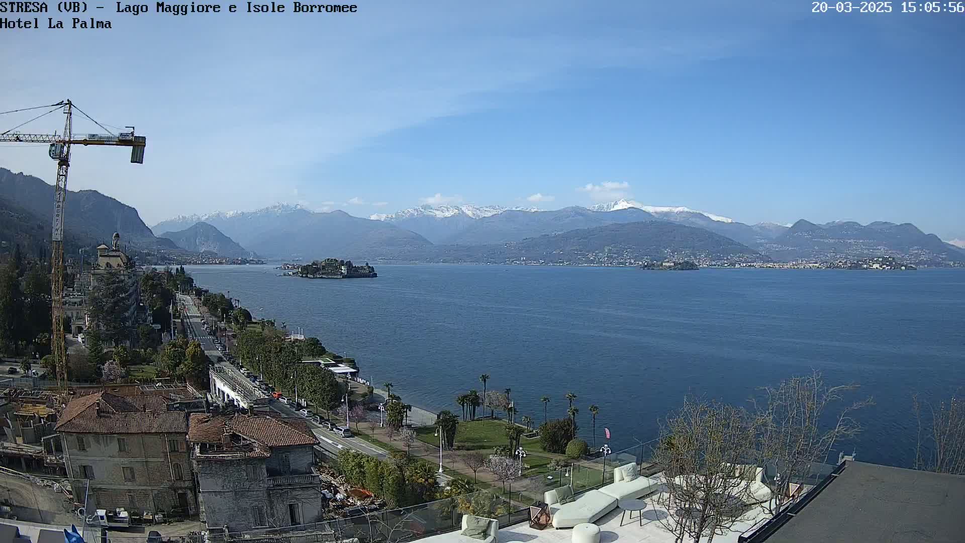 A sunny day reveals a large body of water with snow-capped mountains in the distance, a town along the shoreline, and an island in the foreground.