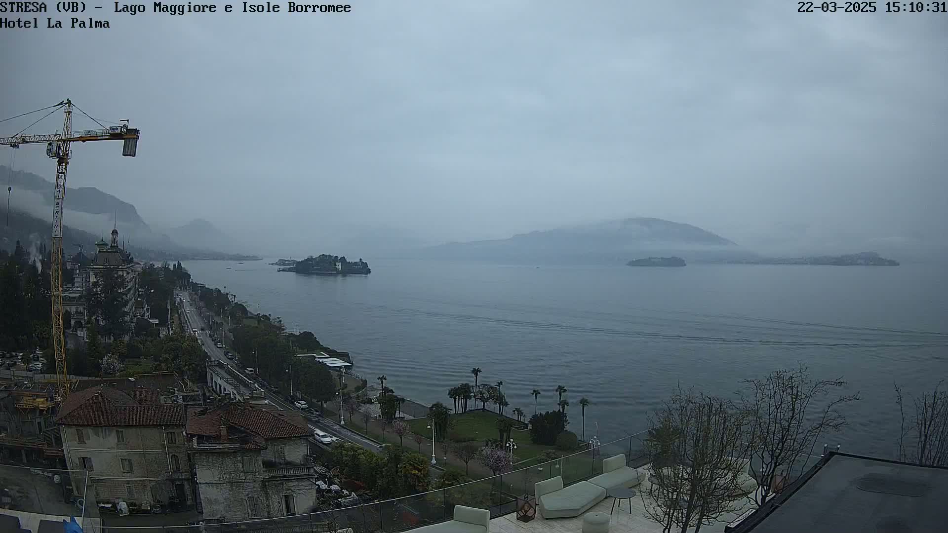 A hazy, overcast day reveals a large body of water with islands in the distance, a town along the shoreline, and a construction crane near buildings.