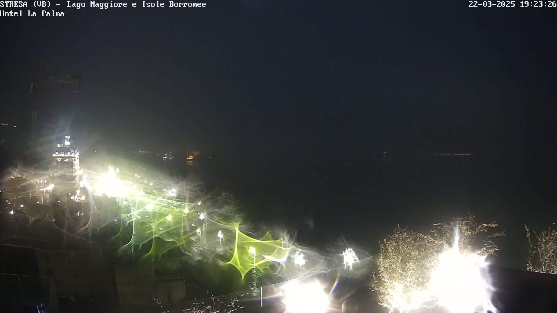 A nighttime long exposure shot shows streaks of light over a body of water, with some vegetation and lights visible in the foreground.