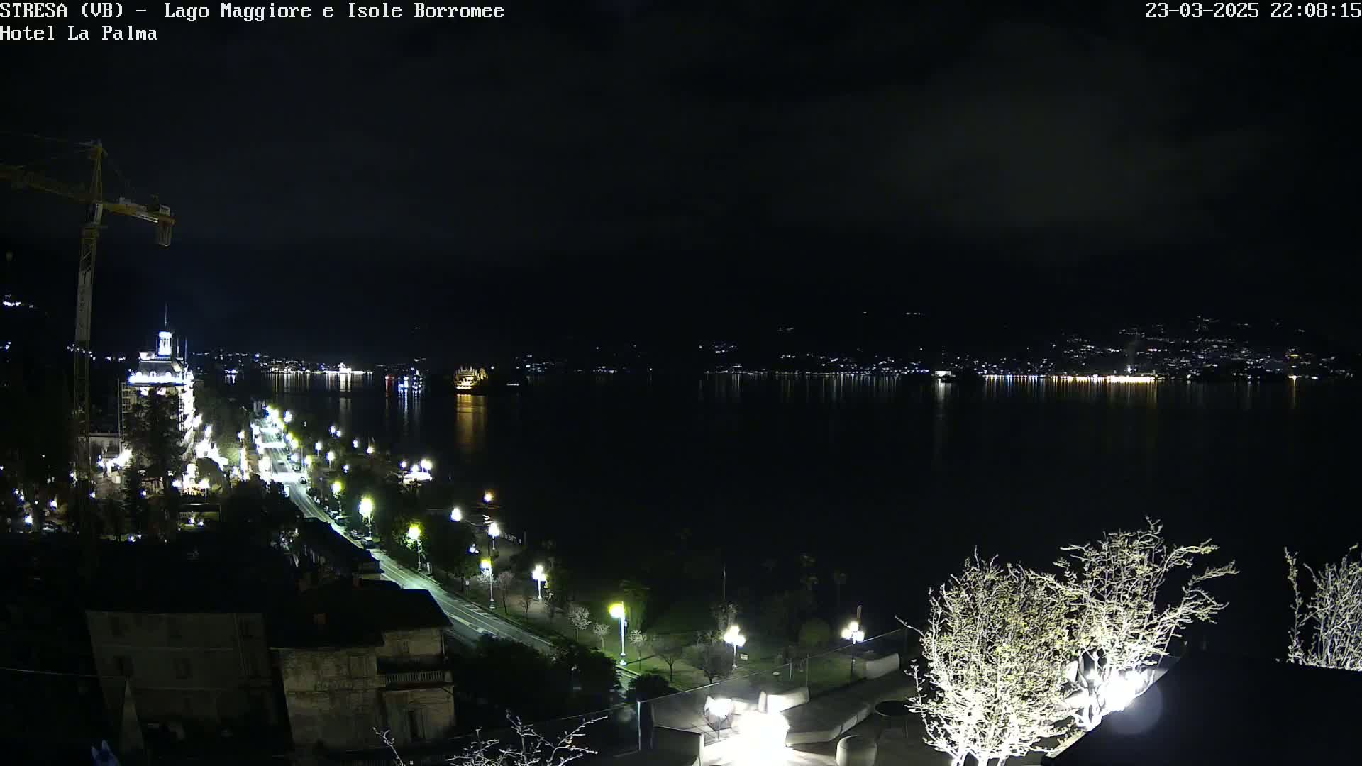 A nighttime view of a city's waterfront, illuminated by streetlights, overlooking a dark lake reflecting distant city lights.