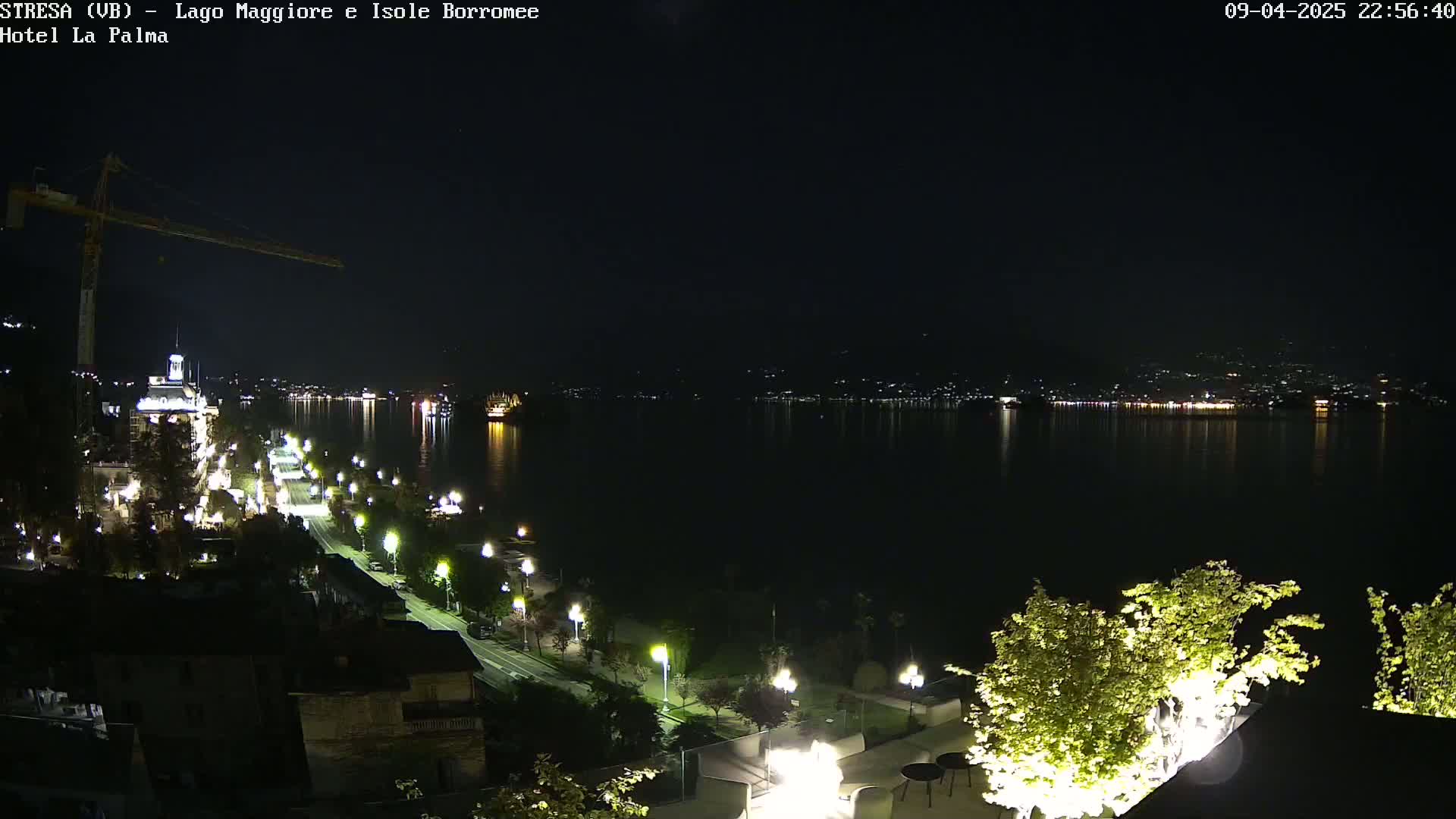 A nighttime view of a city illuminated along a waterfront, overlooking a calm lake with distant city lights reflecting on the water.