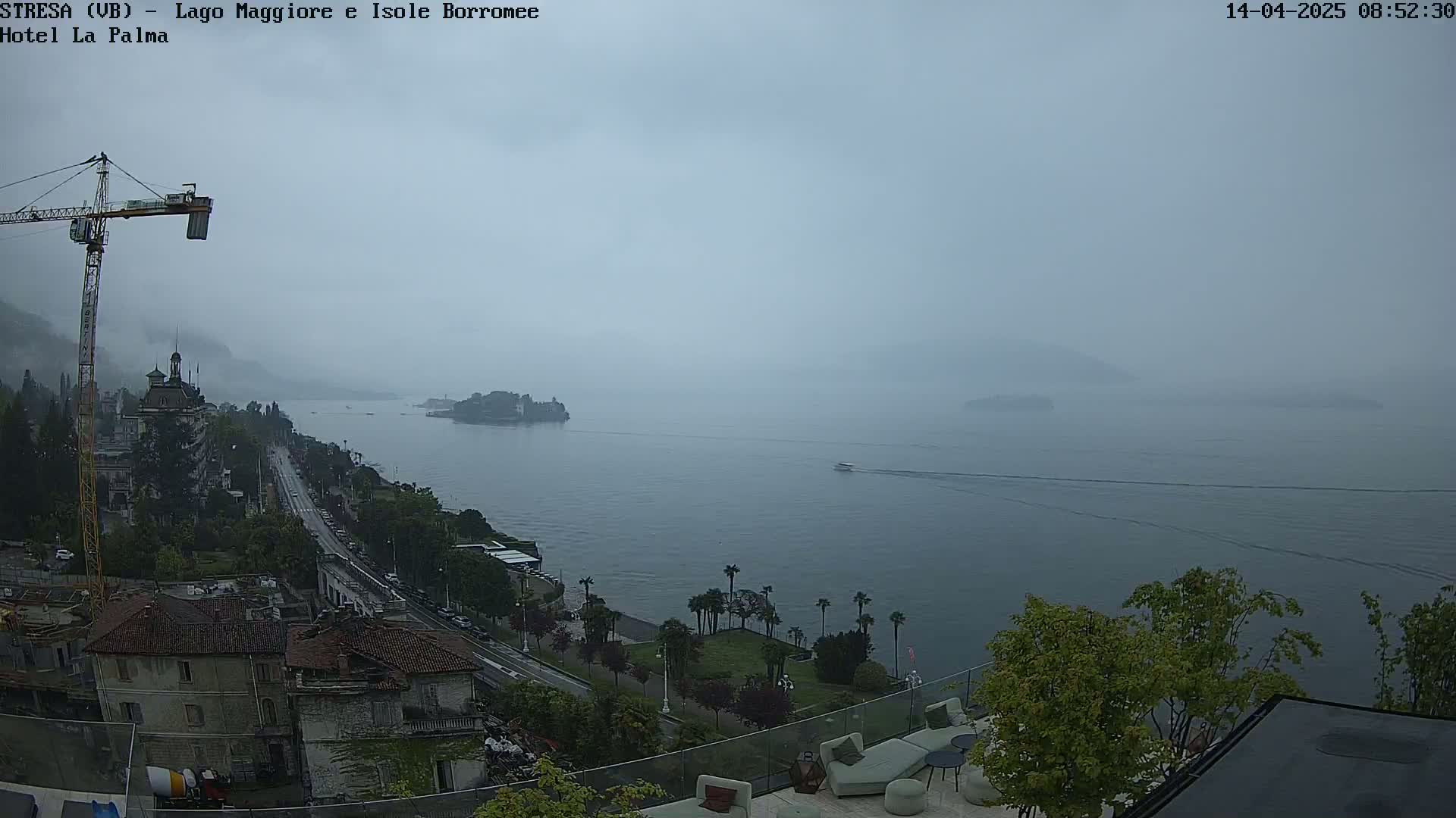 A hazy, overcast view shows a large body of water with small islands in the distance, a town along the shoreline with a construction crane, and a patio area in the foreground.