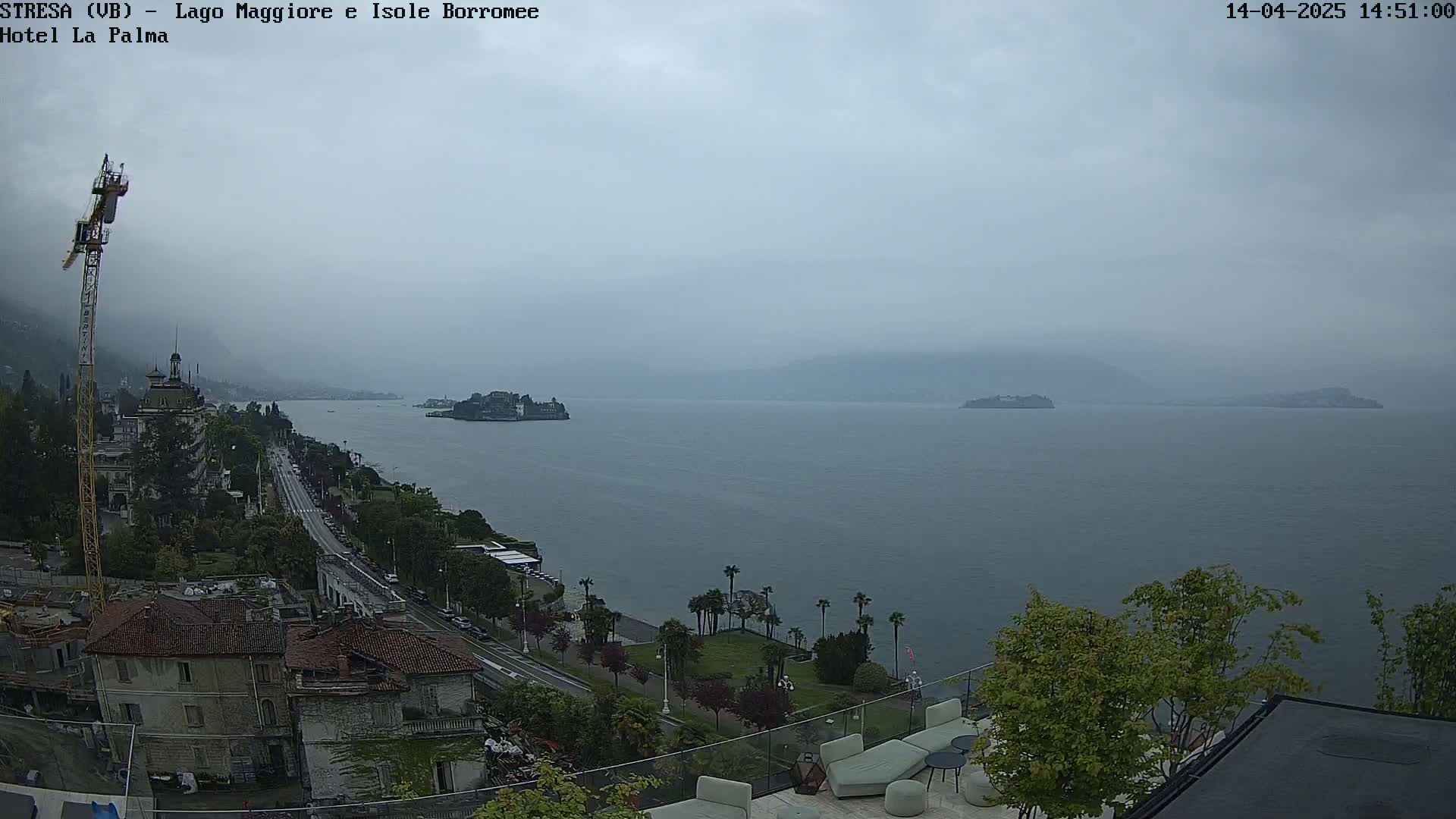A hazy, overcast day reveals a wide expanse of water with islands in the distance, a shoreline lined with buildings and vegetation, and a construction crane visible near the foreground.