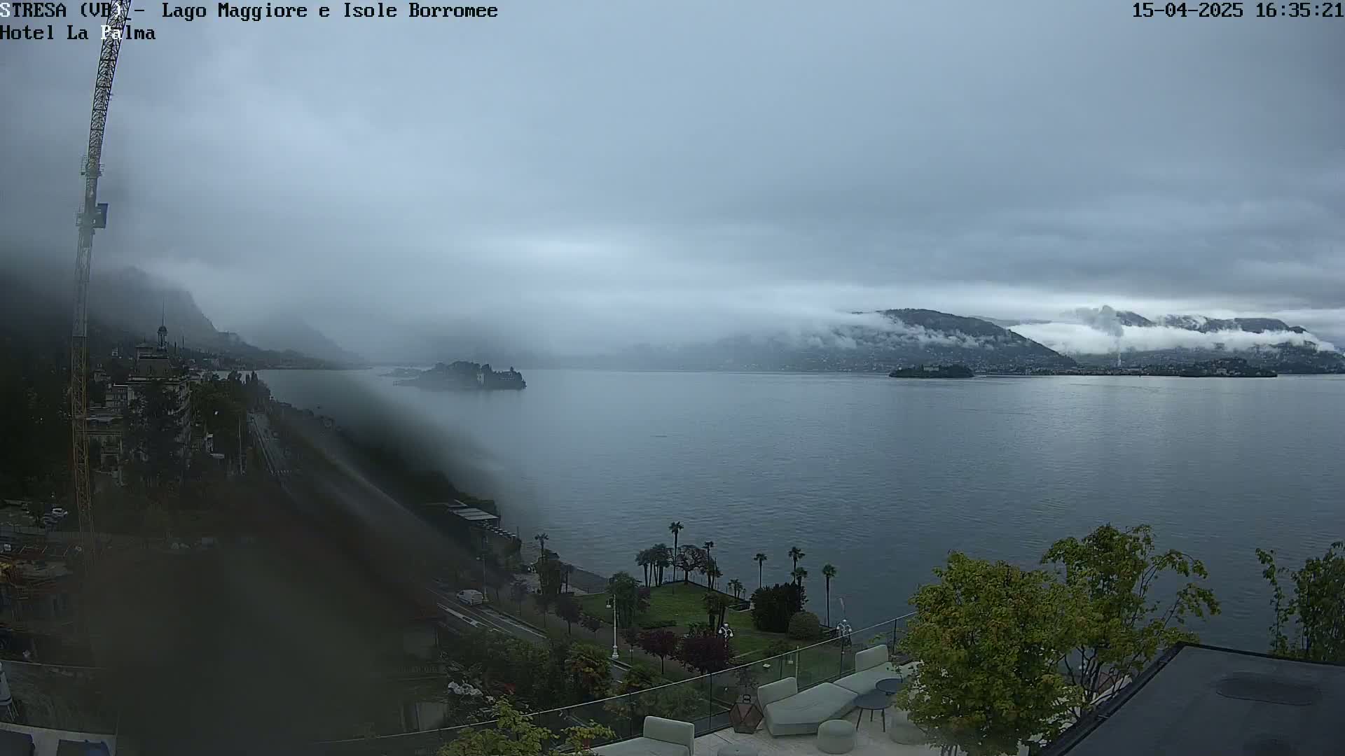 A foggy day overlooks a large body of water with islands and mountains in the distance, viewed from a high vantage point with landscaping and buildings in the foreground.