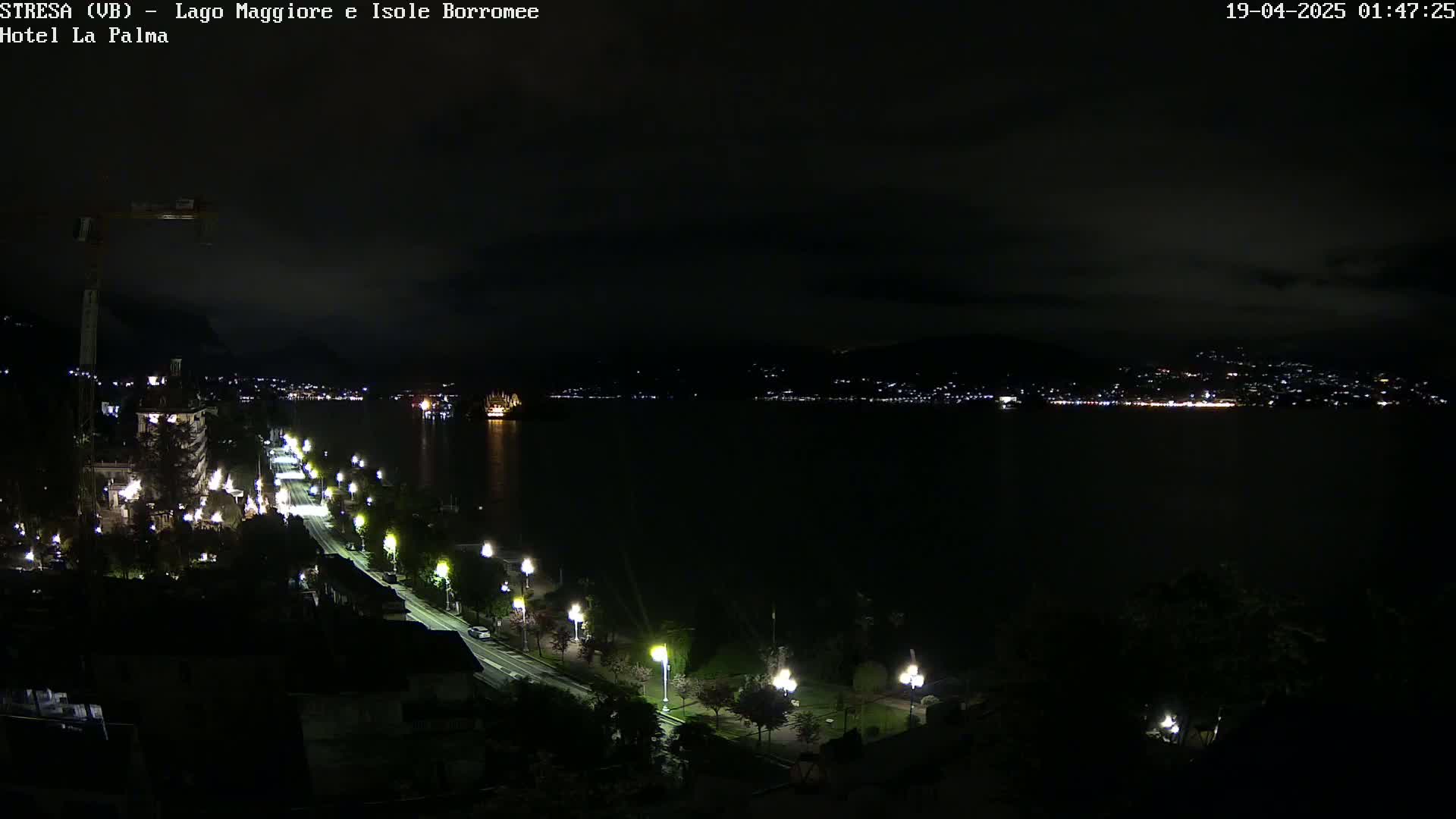 A nighttime view of a dark lake with a city's lights on the far shore and a road lined with lamps along the near shore.