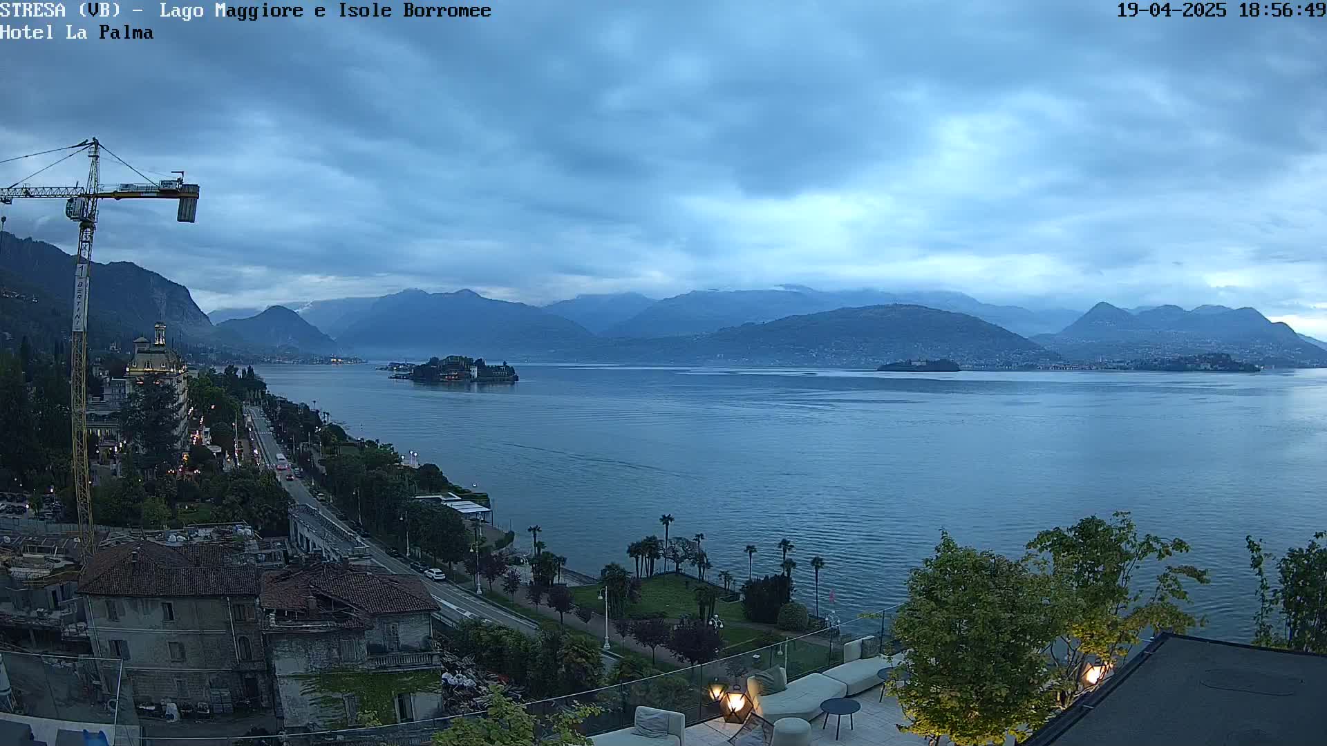 An overcast evening view of a lake and mountains, with a city and a construction crane visible in the foreground.