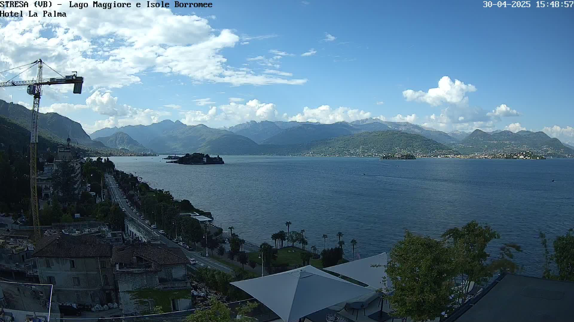 A partly cloudy day overlooks a large lake with islands and distant mountains, as seen from a high vantage point near buildings and vegetation.