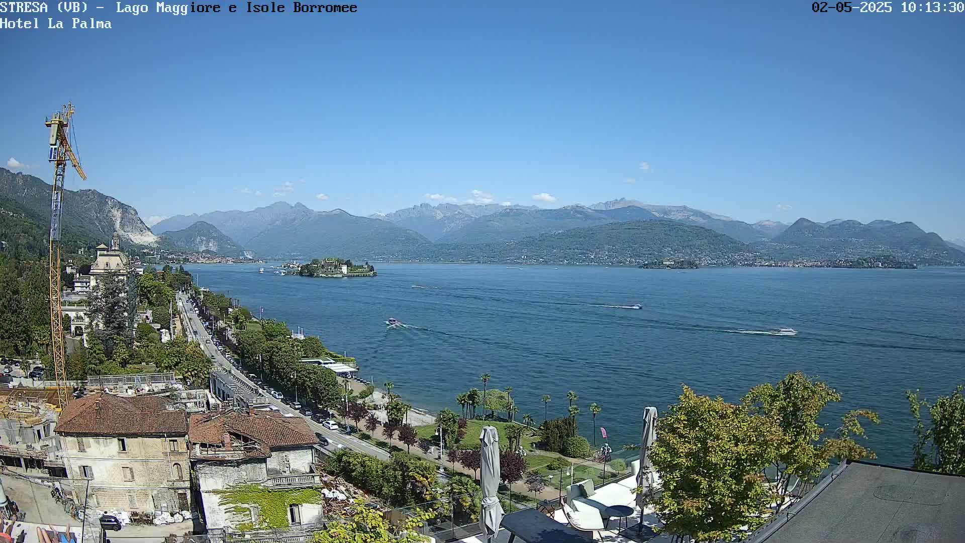 A sunny day overlooking a lake with mountains in the distance, a shoreline with buildings and trees, and several boats on the water.