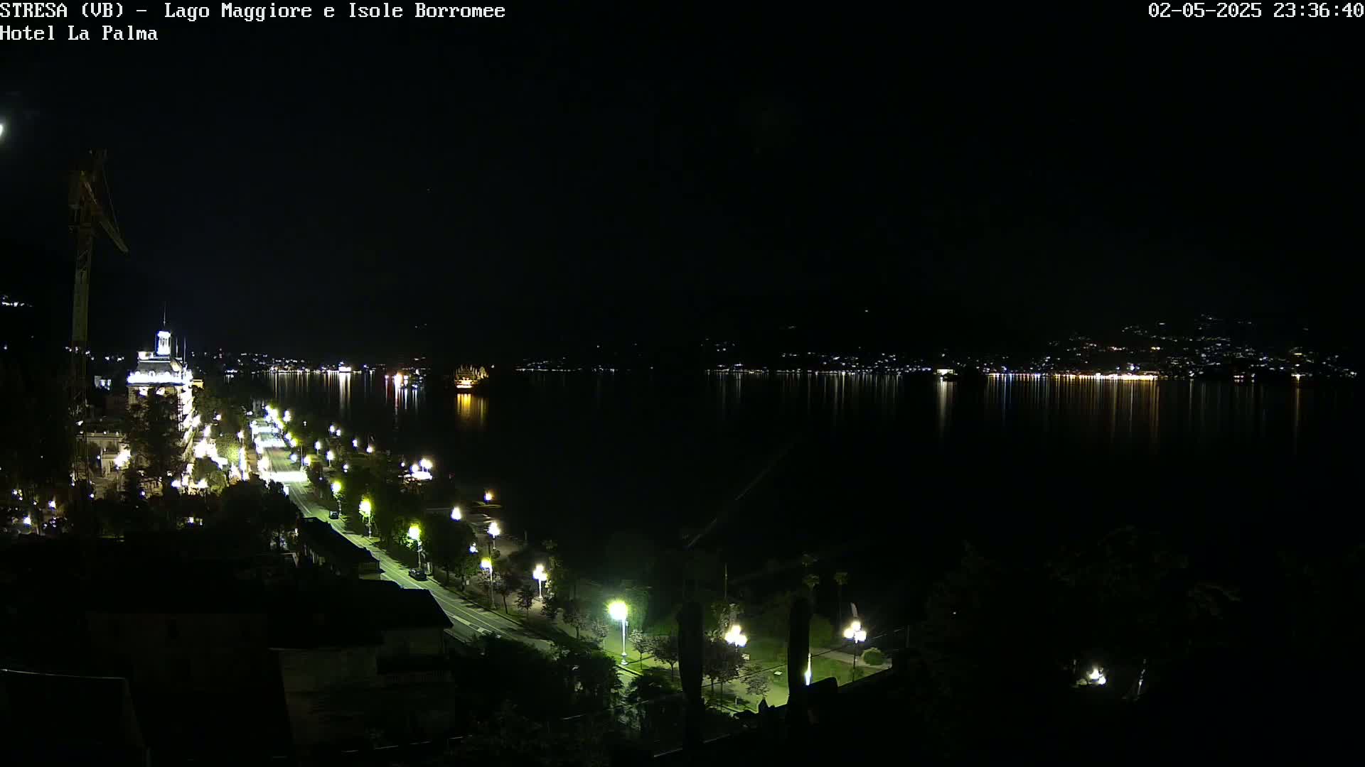 A nighttime view of a city illuminated along a waterfront, with calm waters reflecting the lights across a dark lake.