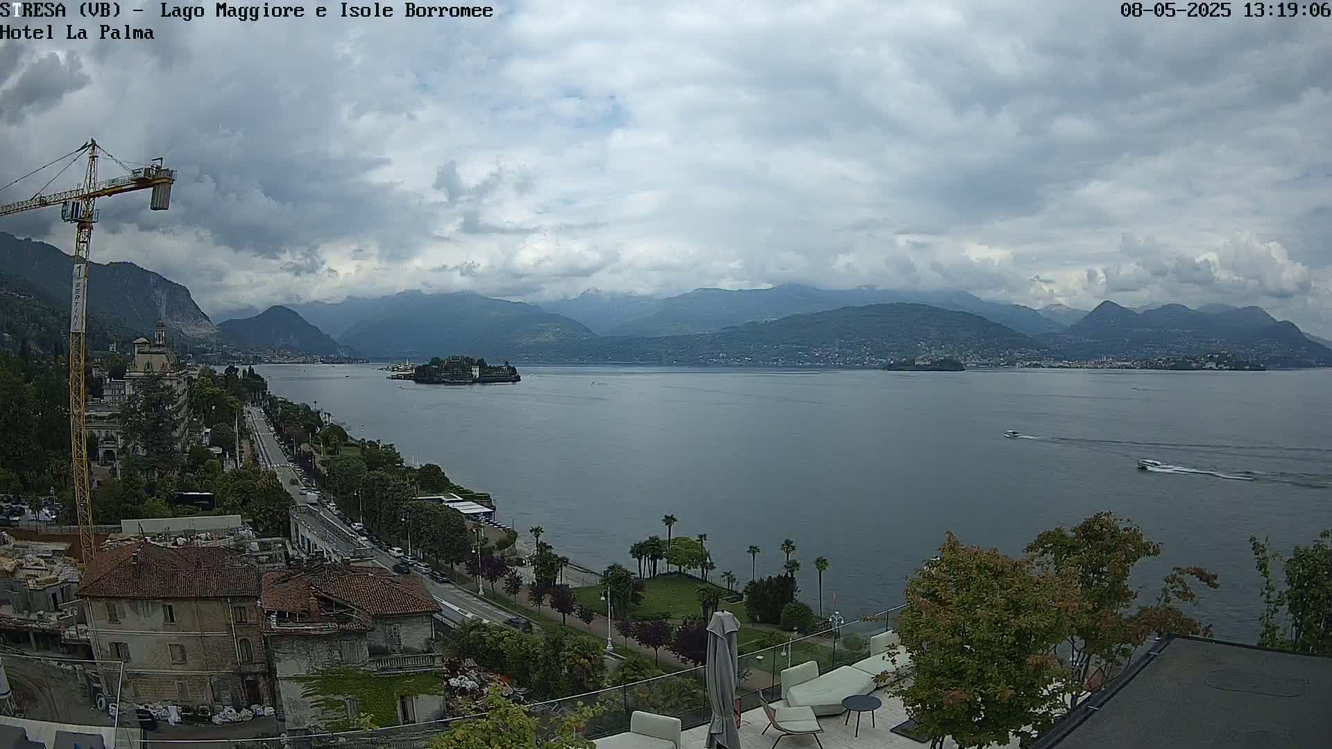 A cloudy day overlooking a large lake with mountains in the distance, a small island in the lake, and buildings along the lakeshore.