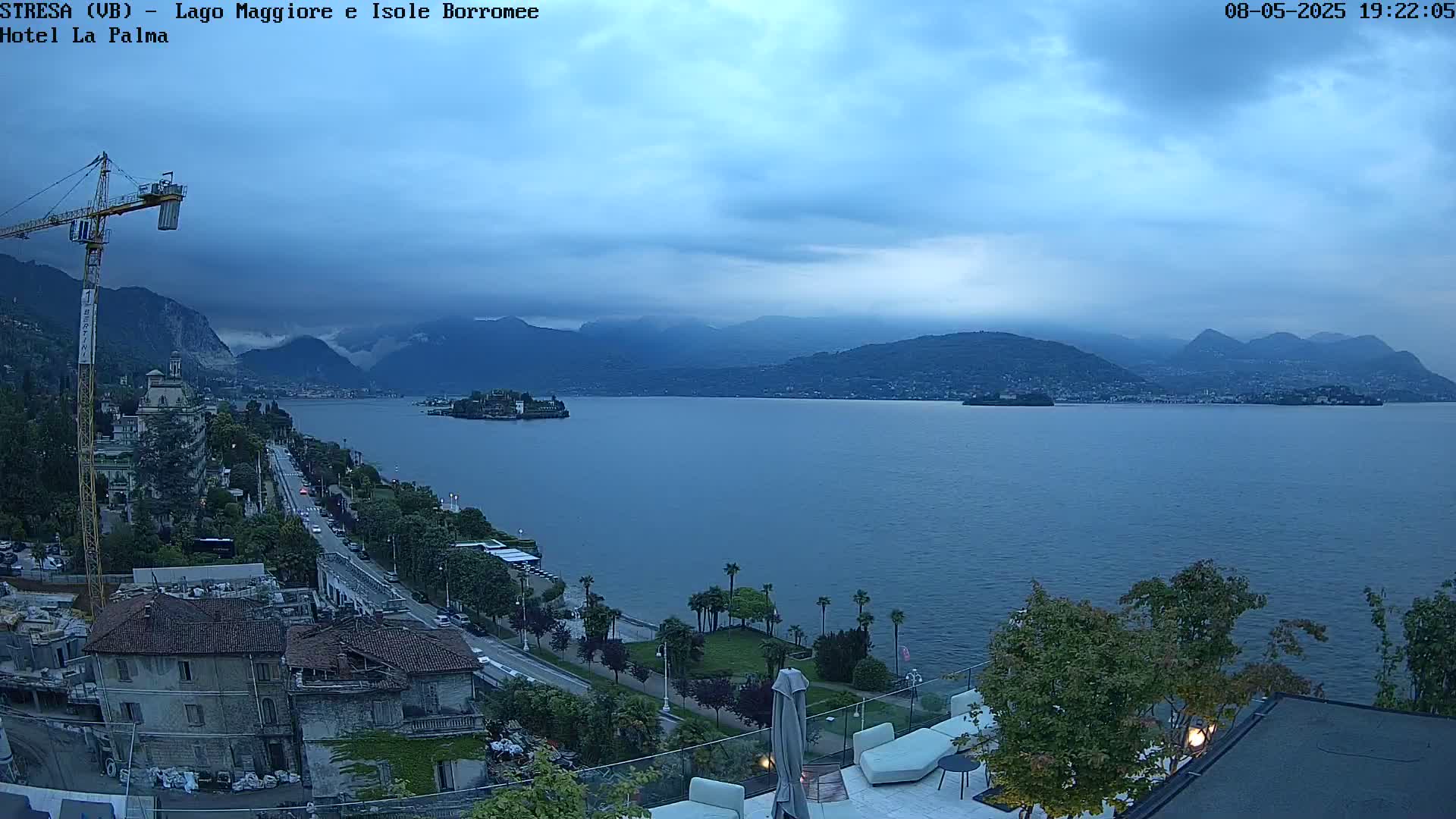 A tranquil lake scene at dusk, under a cloudy sky, shows a town nestled along the shoreline with mountains in the distance and a small island in the lake.