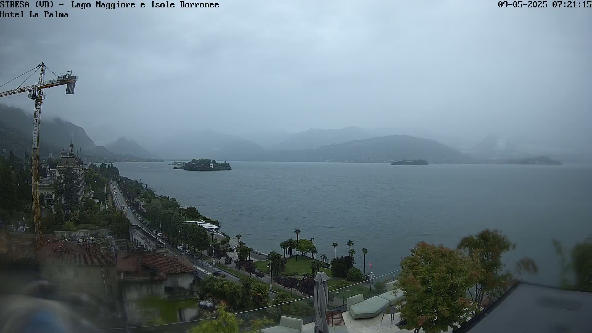 A hazy, overcast day reveals a large lake with distant mountains and islands, viewed from an elevated position overlooking a roadway and a hotel patio.