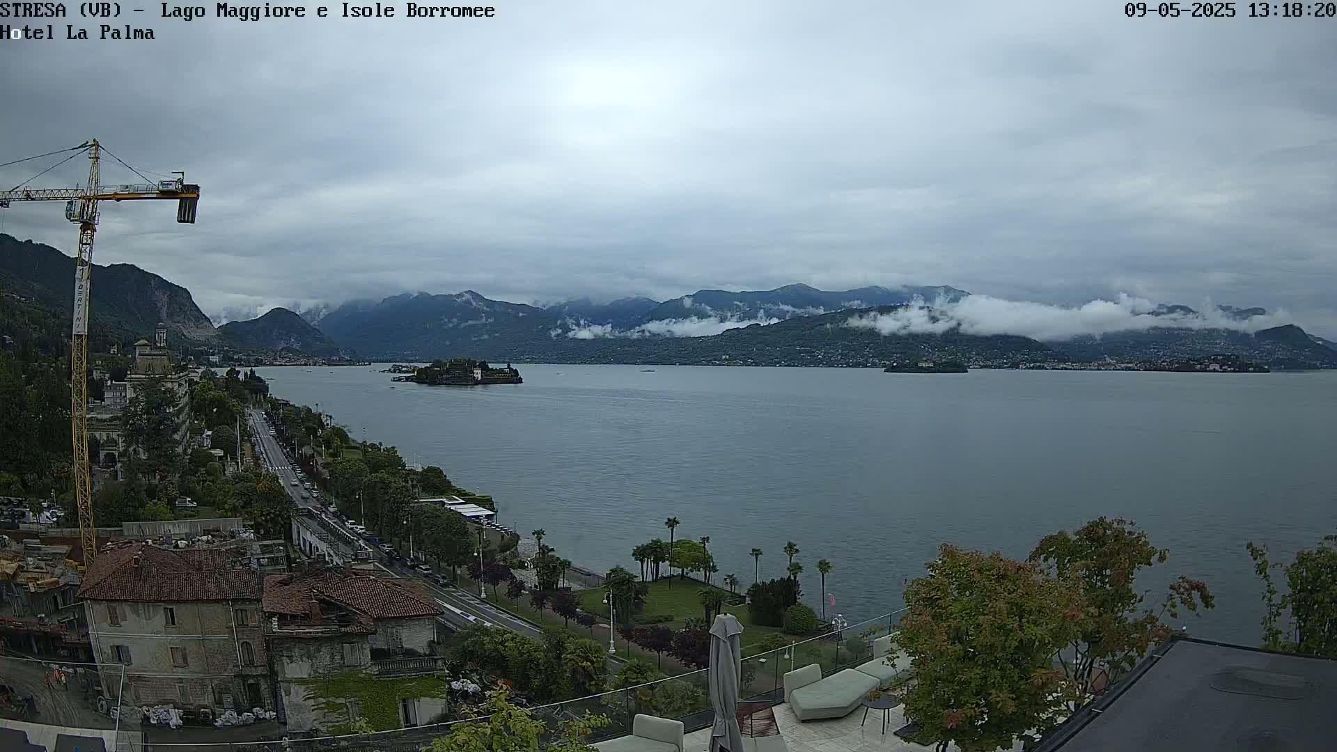 A view from a rooftop overlooking a calm lake, with distant mountains shrouded in clouds and a cityscape along the shoreline, under an overcast sky.