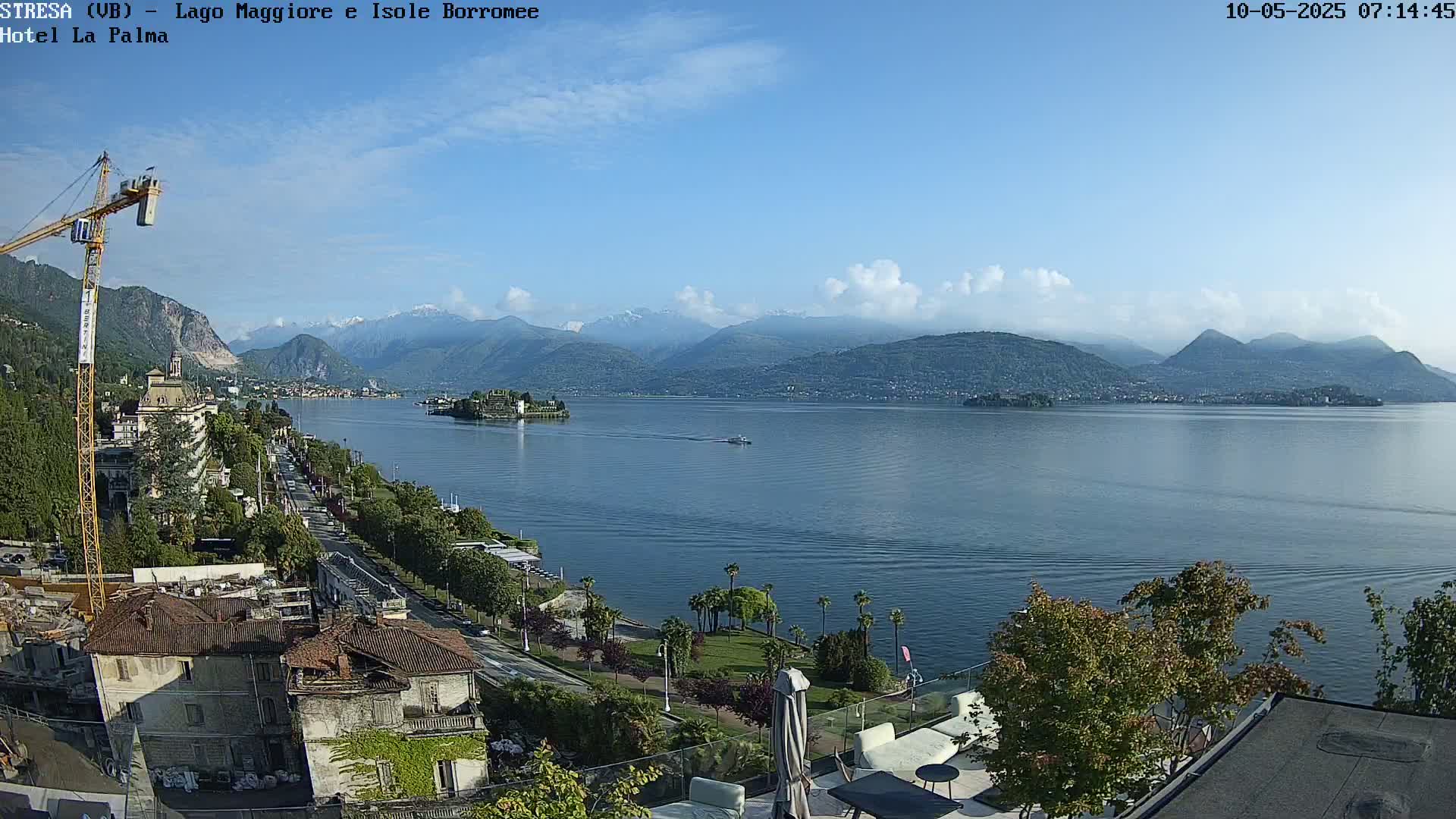 A partly cloudy day overlooking a lake with mountains in the background, a small island in the foreground, and a town visible along the shoreline.