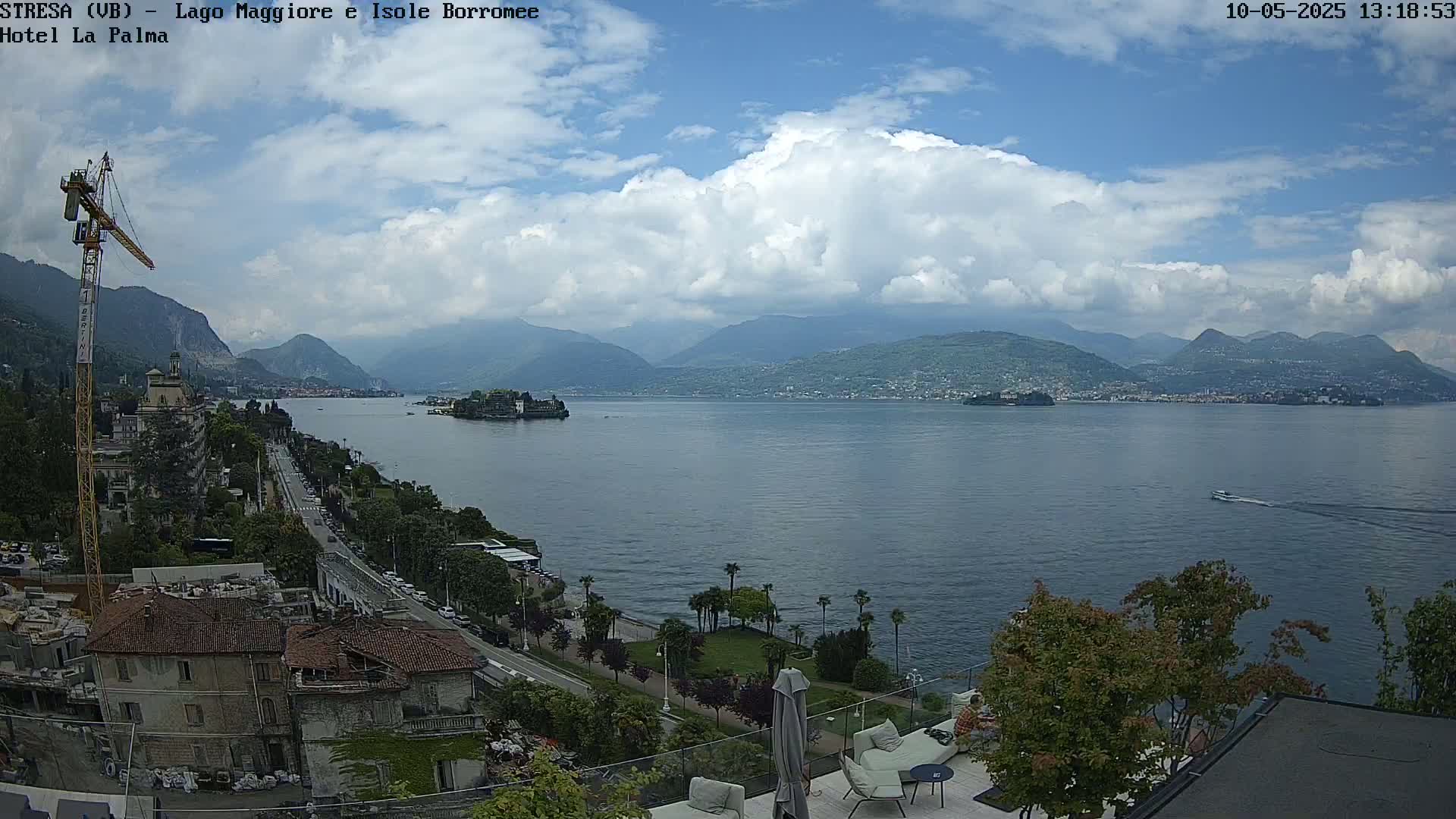 A partly cloudy day overlooking a lake with mountains in the distance, a town along the shore, and a small island in the lake.