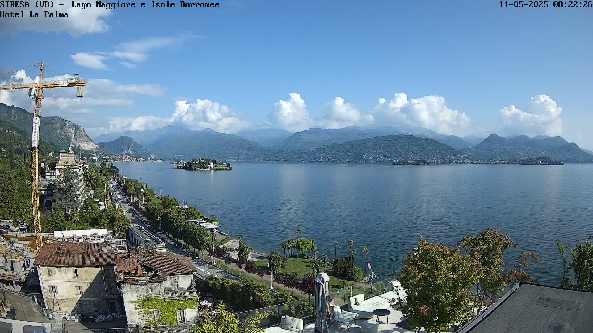 A partly cloudy day overlooks a lake with distant mountains, a town, and an island, all viewed from an elevated position near a building under construction.