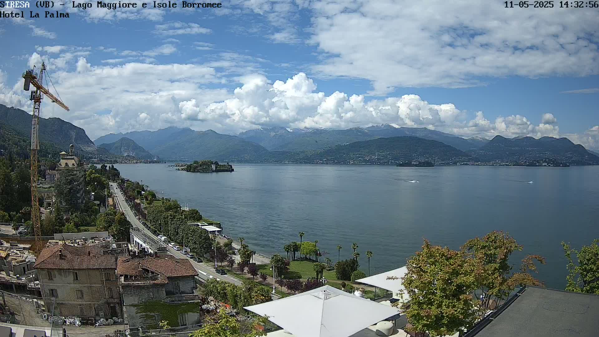 A partly cloudy day overlooks a lake with mountains in the background, a construction crane and buildings are visible in the foreground.