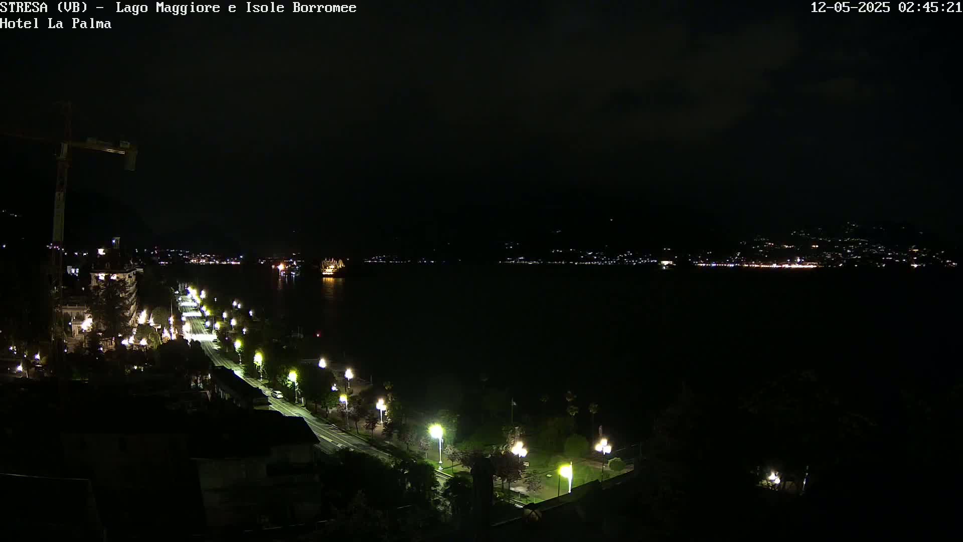 A nighttime view of a city's waterfront illuminated by streetlights along a road leading to a dark body of water with lights visible on the opposite shore.