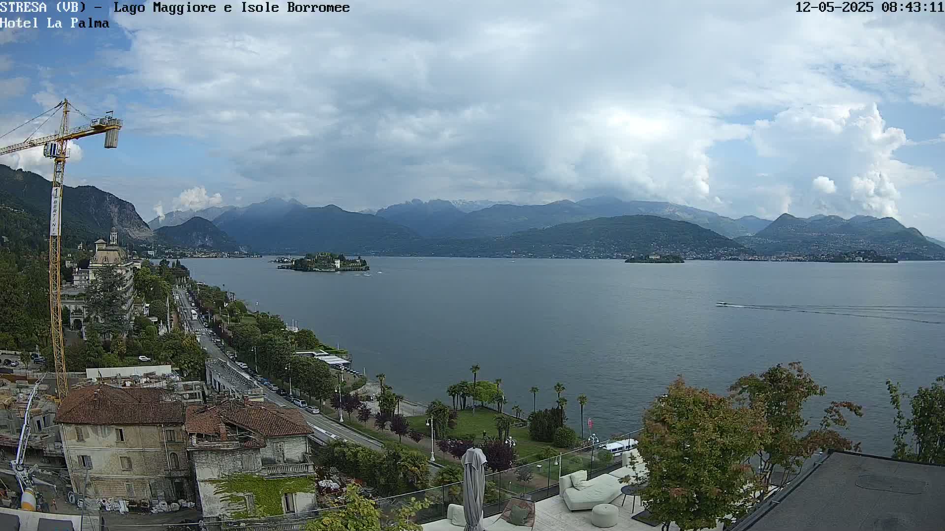 A partly cloudy day overlooking a large lake with islands and mountains in the distance, featuring a crane and buildings along the lakeshore.