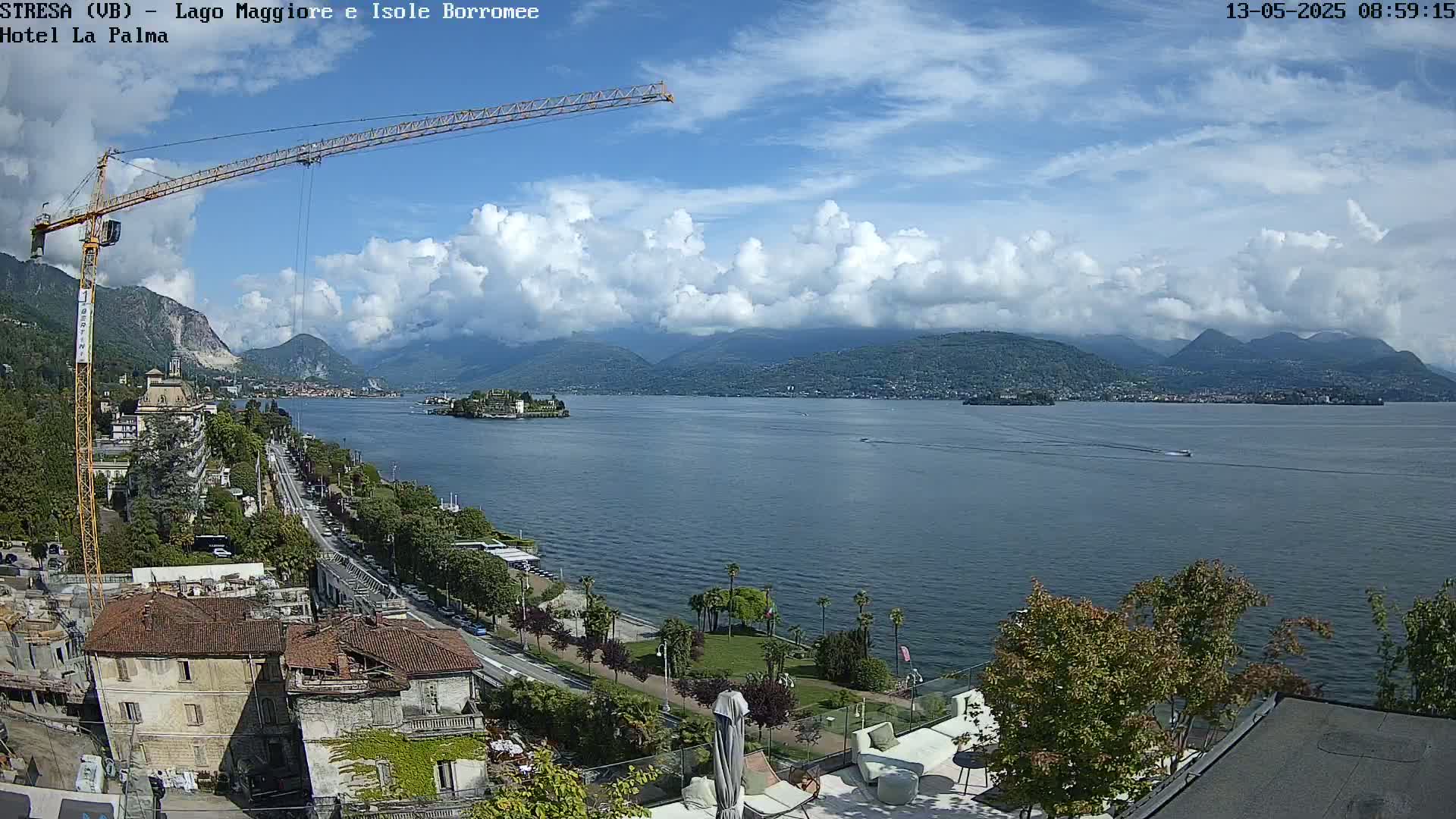A partly cloudy day overlooks a large body of water with mountains in the background, a crane, and buildings along the shoreline.
