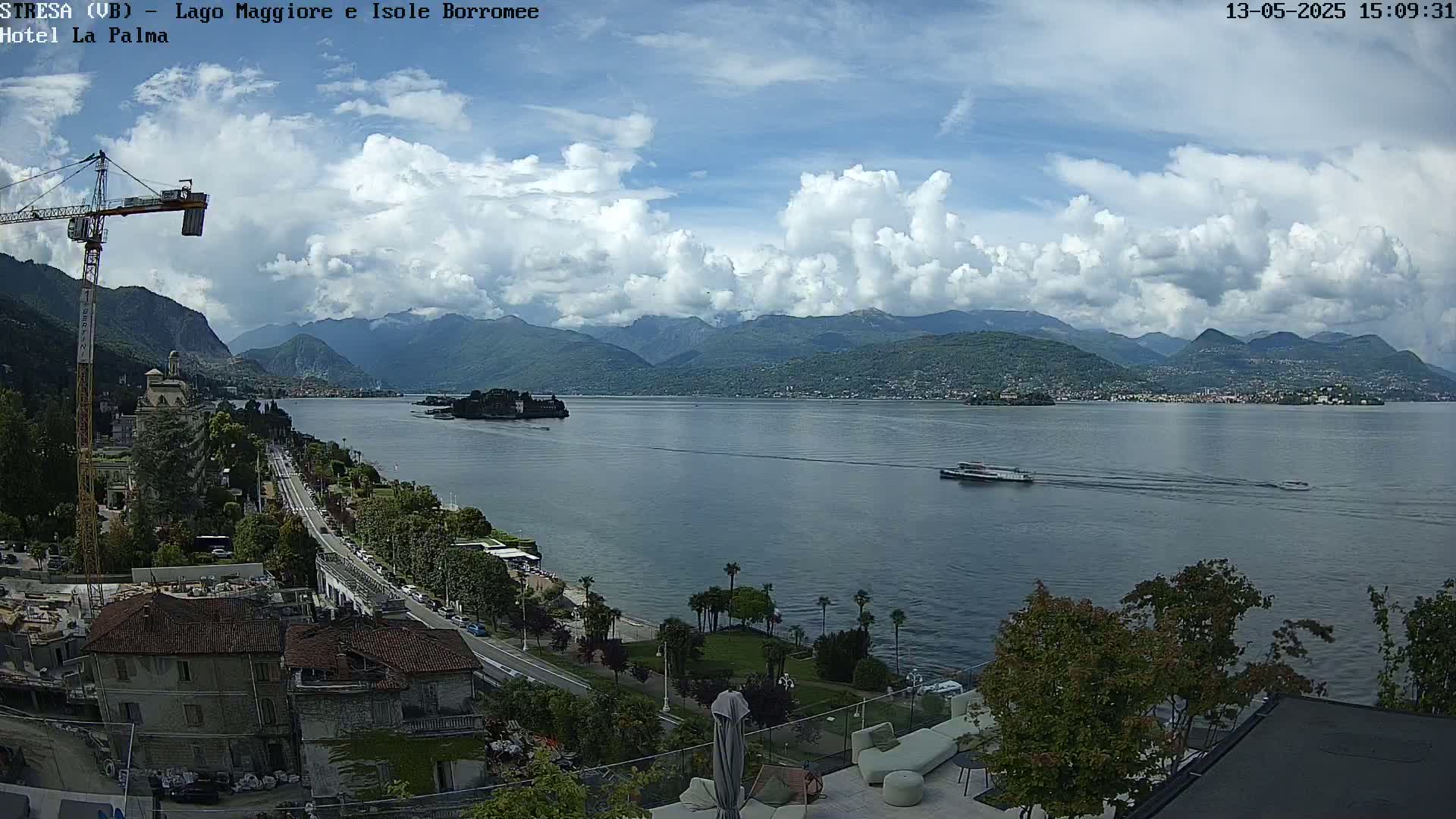 A partly cloudy day reveals a large lake with mountains in the background, a boat on the water, and a town stretching along the lake's edge.