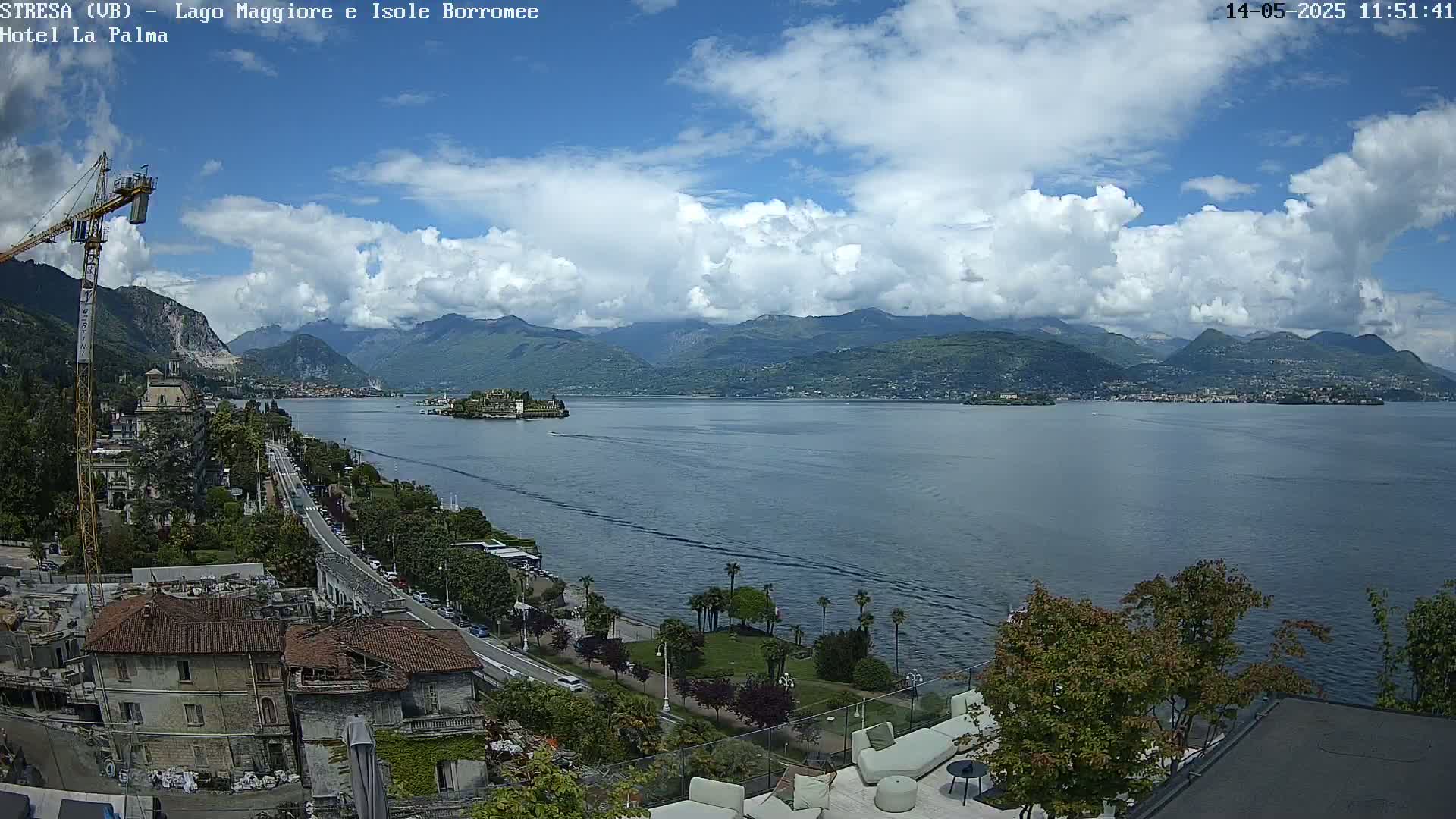 A partly cloudy day overlooking a lake with mountains in the background, a town on the lakeshore, and a construction crane visible in the foreground.