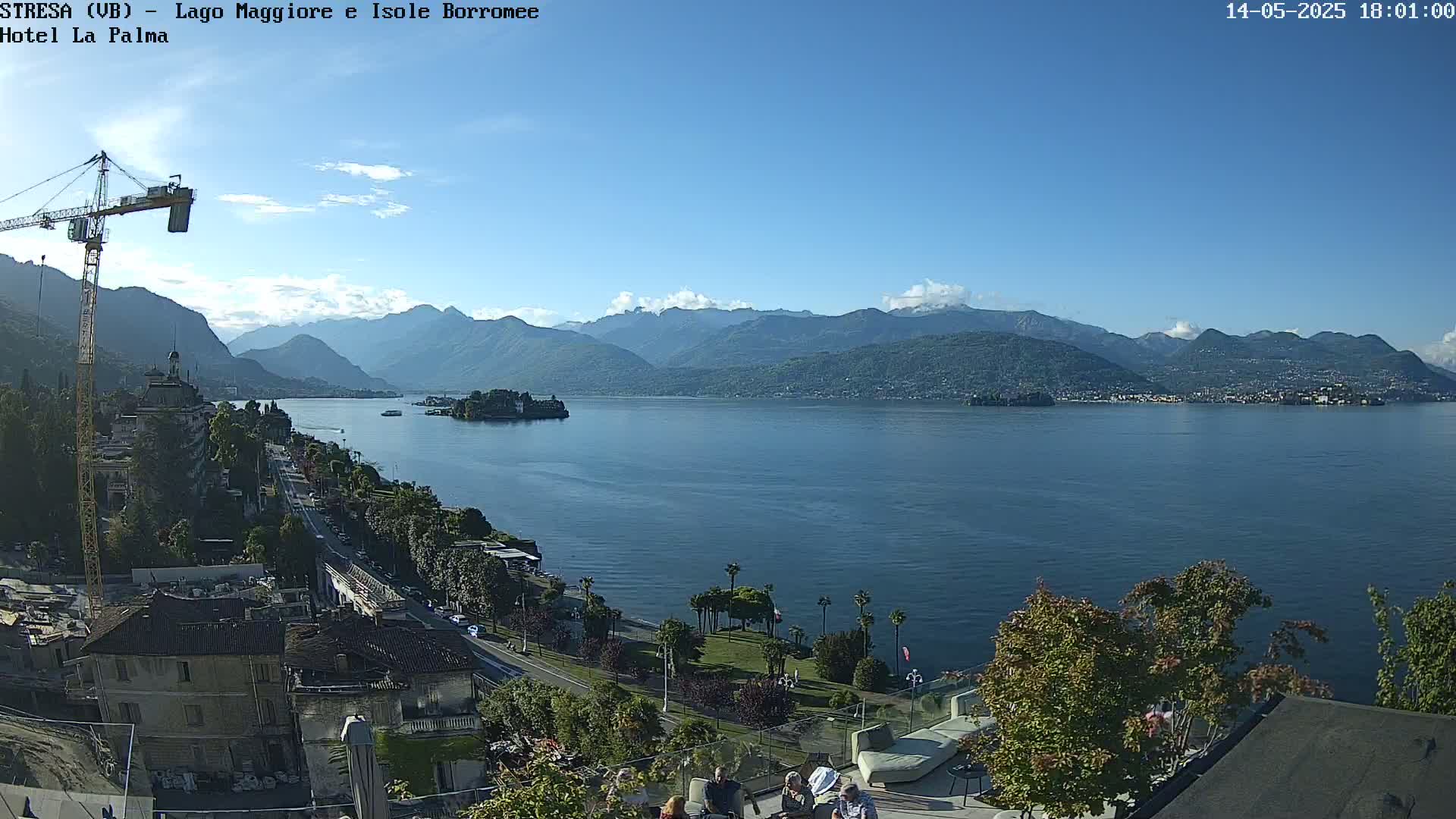 A sunny day overlooking a large lake with mountains in the background, a town on the lakeshore, and a construction crane visible near buildings.