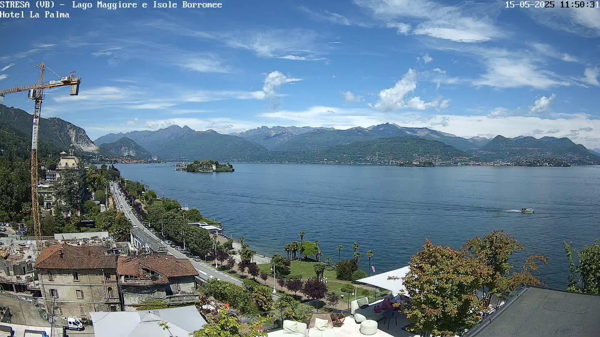 A sunny day overlooks a large lake with mountains in the background, a small island in the middle of the lake, and a town along the shoreline with construction visible.