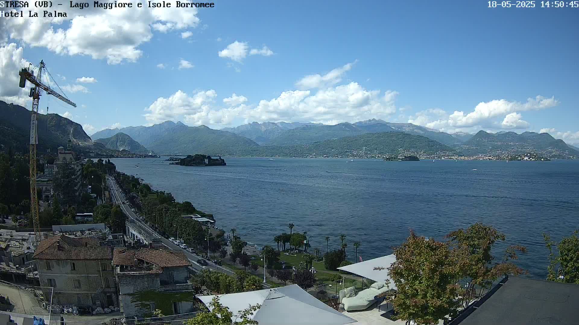 A partly cloudy day overlooking a large lake with mountains in the background, a town visible along the shoreline, and construction visible near the foreground.
