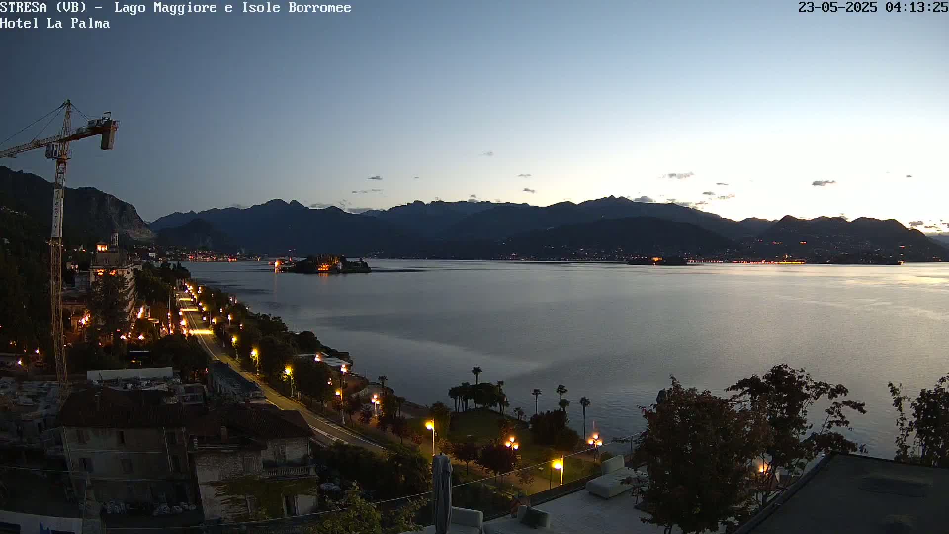 A nighttime view of a lake, city lights, and mountains under a twilight sky.