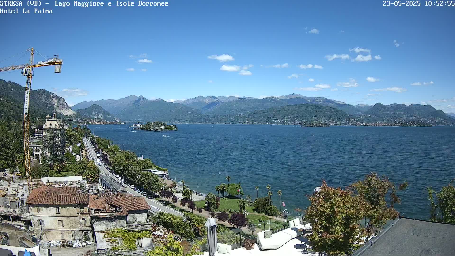 A sunny day overlooking a large lake with mountains in the background, a small island visible in the middle distance, and a seaside town with buildings and a roadway along the shore.