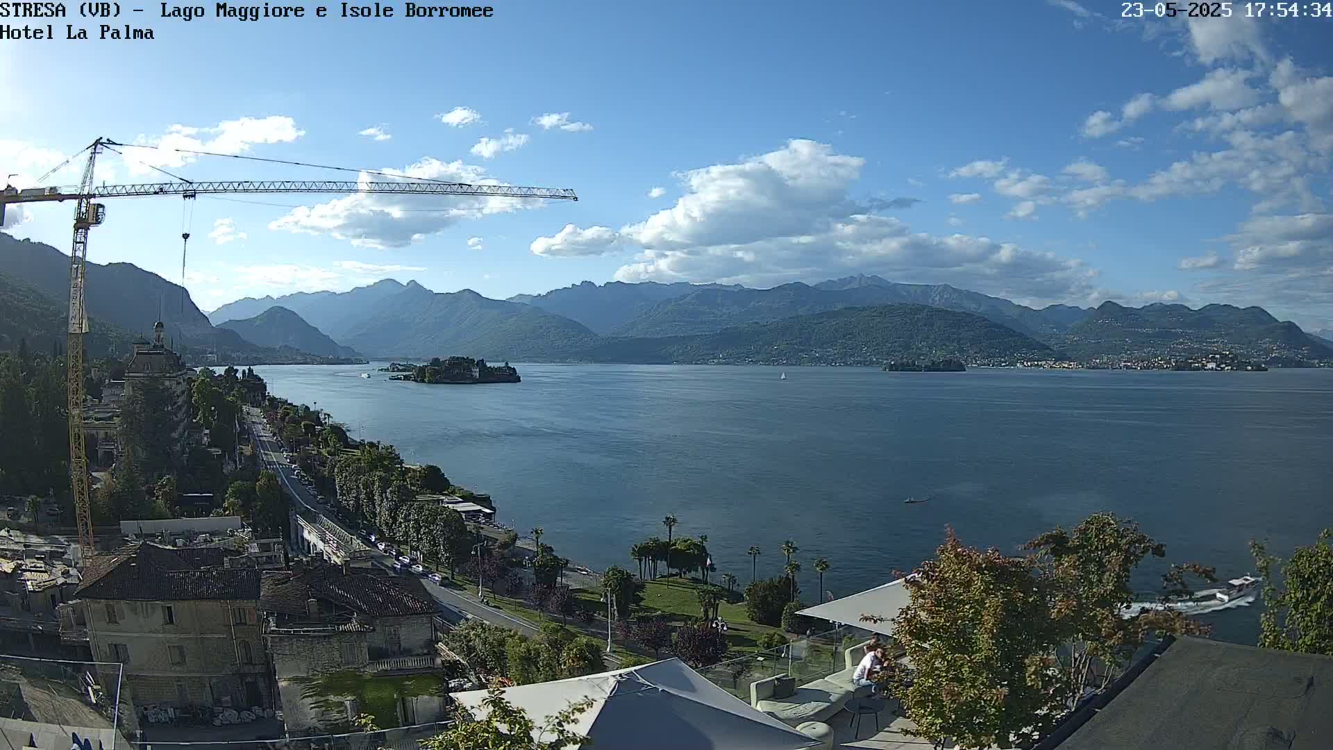 A partly cloudy day overlooking a lake with mountains in the background, a town and a construction crane visible in the foreground.