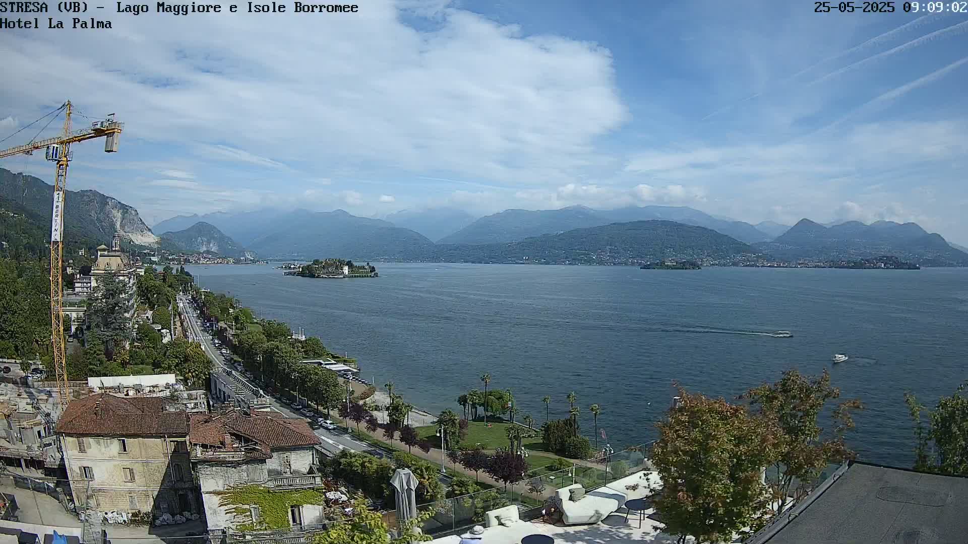 A sunny day overlooking a lake with mountains in the background, a town visible along the shoreline, and a construction crane in the foreground.