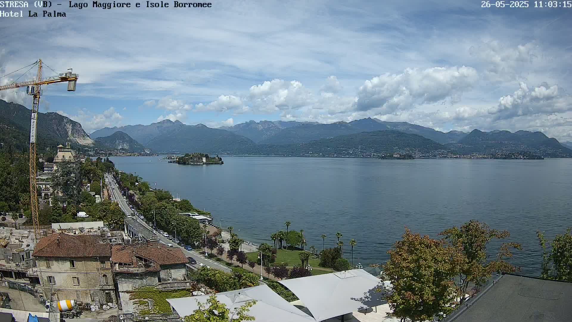 A partly cloudy day overlooks a lake with mountains in the distance, a town along the shoreline, and construction underway near the foreground.