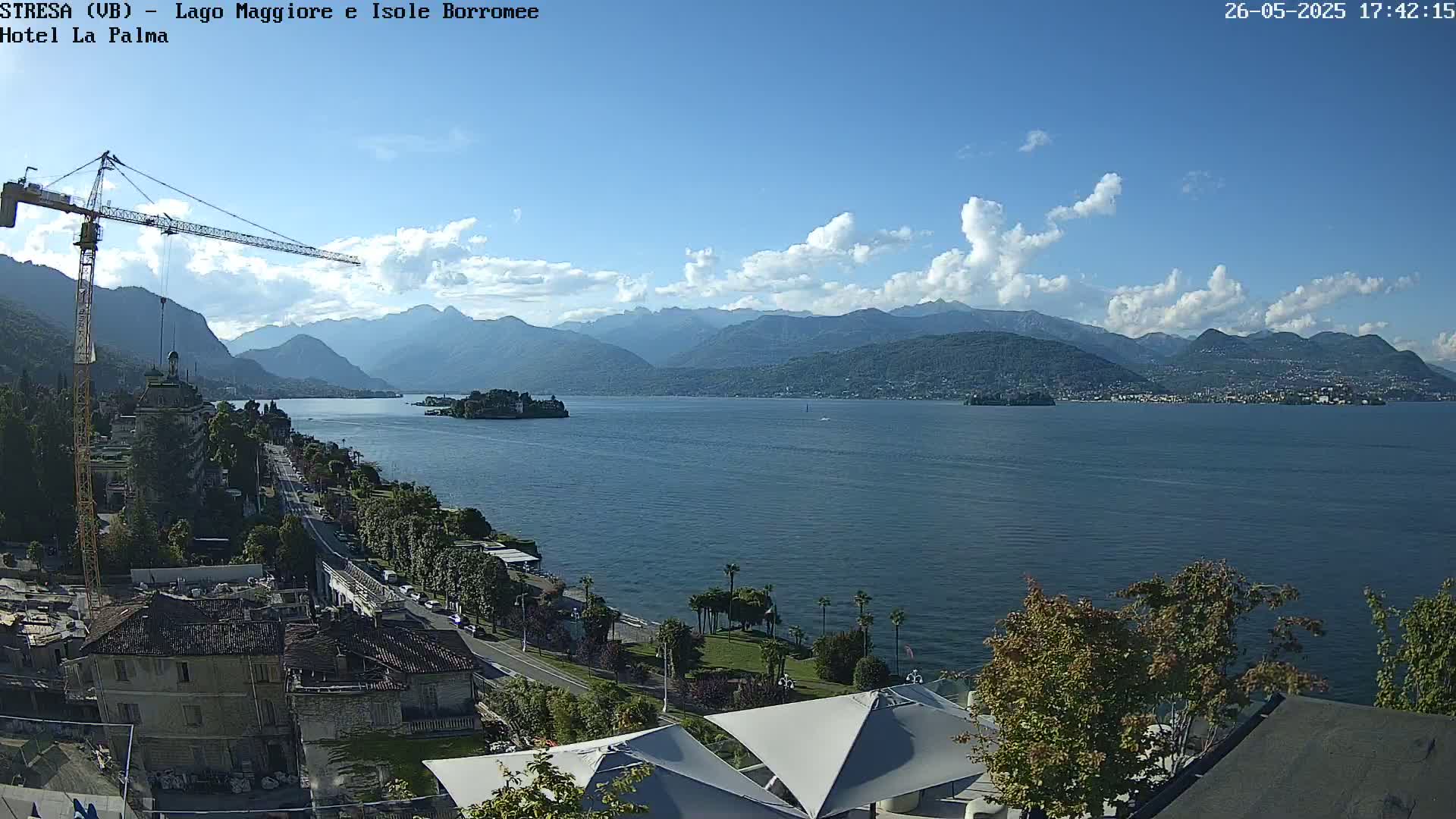 A partly cloudy day overlooking a large lake with mountains in the background, a town along the shoreline, and a construction crane visible.
