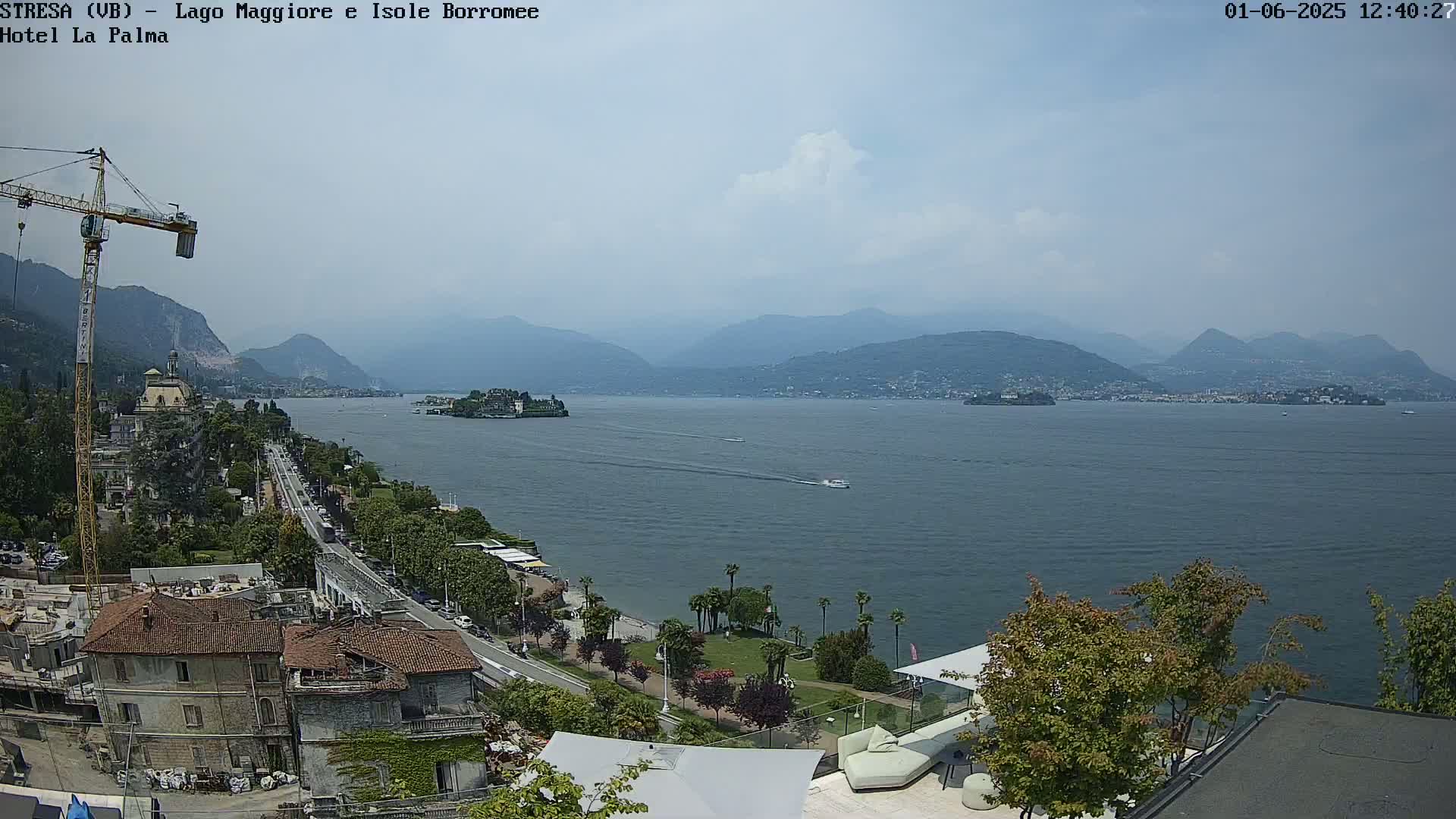 A partly cloudy day overlooking a large lake with mountains in the background, a town along the shoreline, and a construction crane visible.